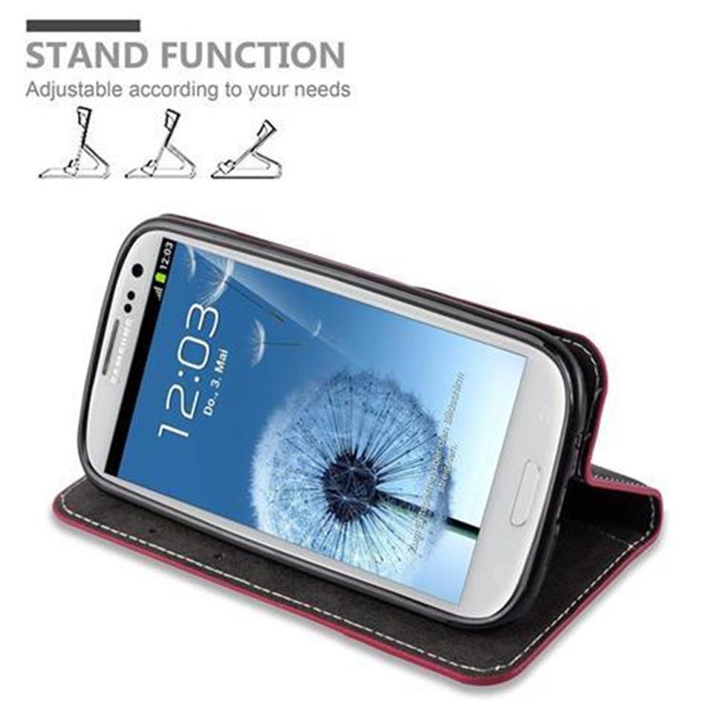 Ein Telefon in einer Hülle, hochgestellt. Die Hülle ist rot und schwarz, das Telefon zeigt die Zeit.