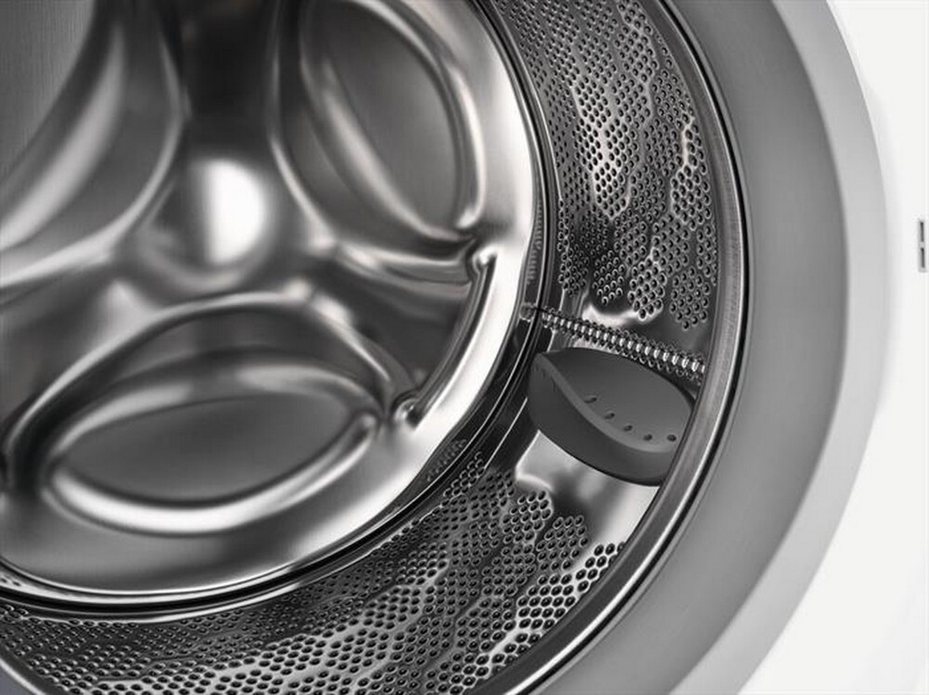 Primo piano dell'interno del cestello di una lavatrice. Acciaio inox perforato con paletta grigia.