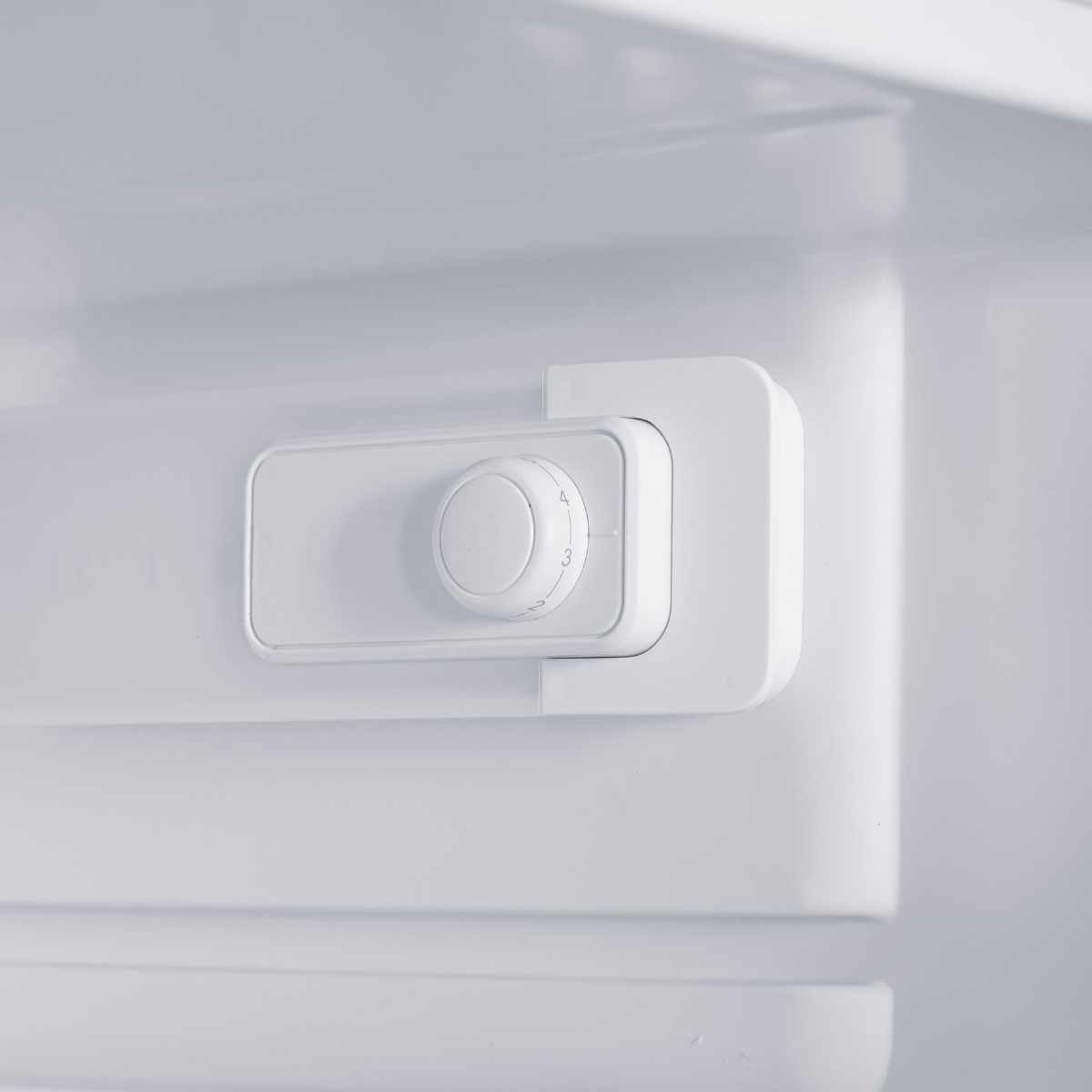 A close-up of a white refrigerator interior with a temperature control dial.