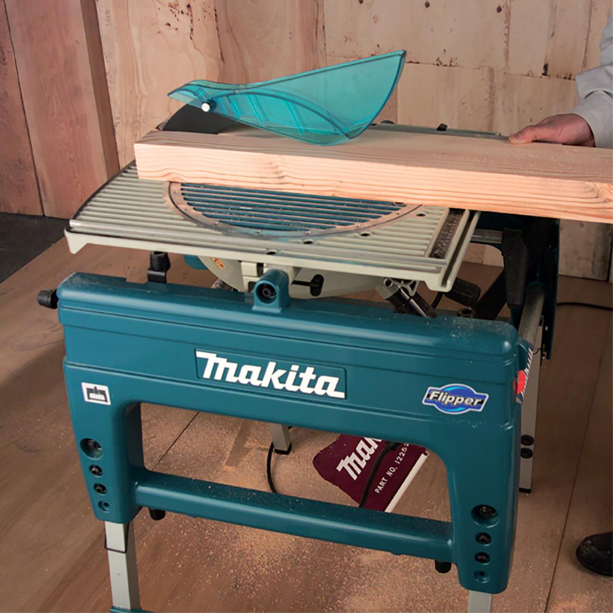 Una sierra de mesa Makita turquesa con madera y protector.