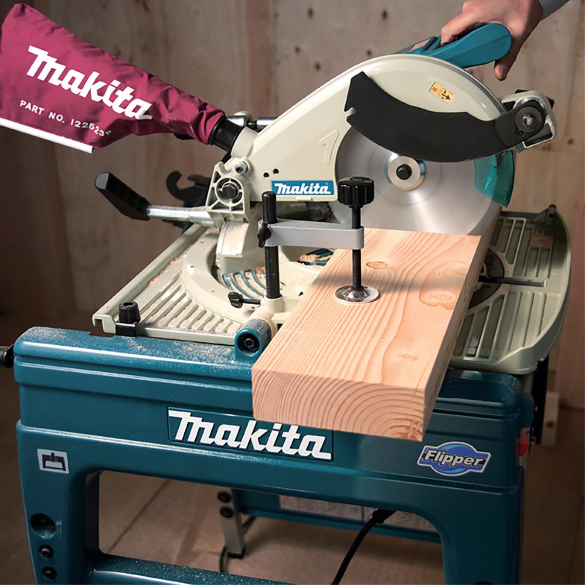 Sierra ingletadora Makita cortando una tabla de madera sobre un soporte turquesa, con la marca Makita visible.