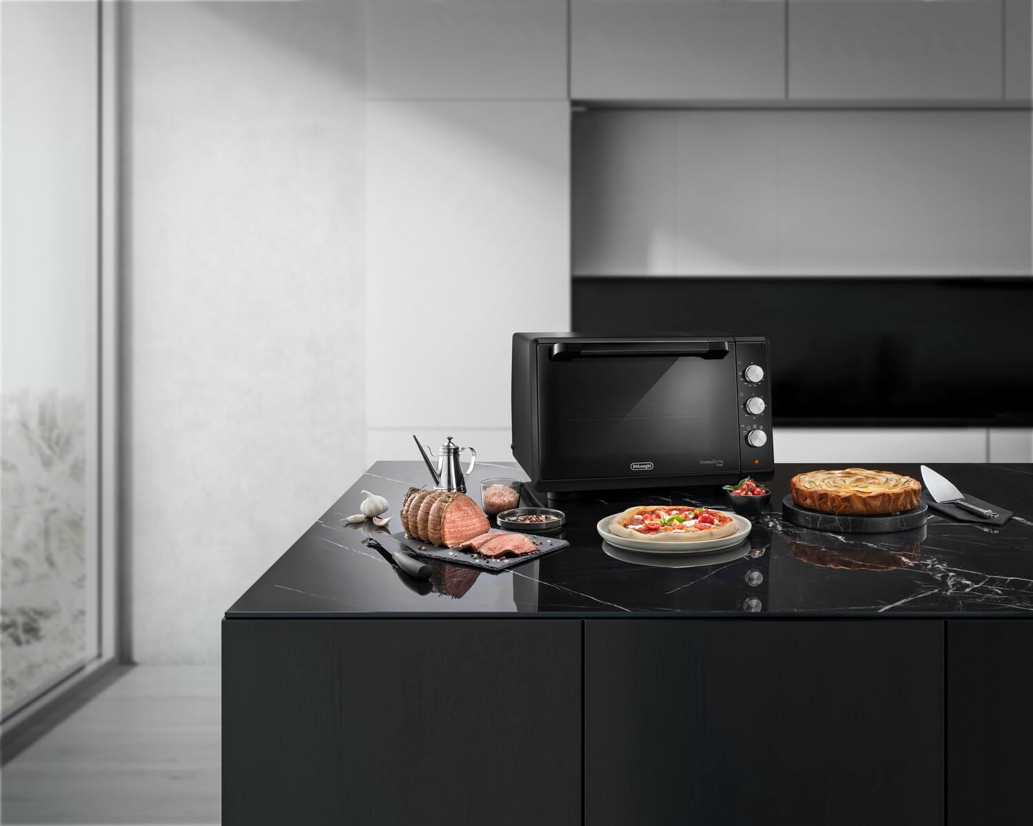 Un forno Delonghi nero su un piano di lavoro nero con generi alimentari.