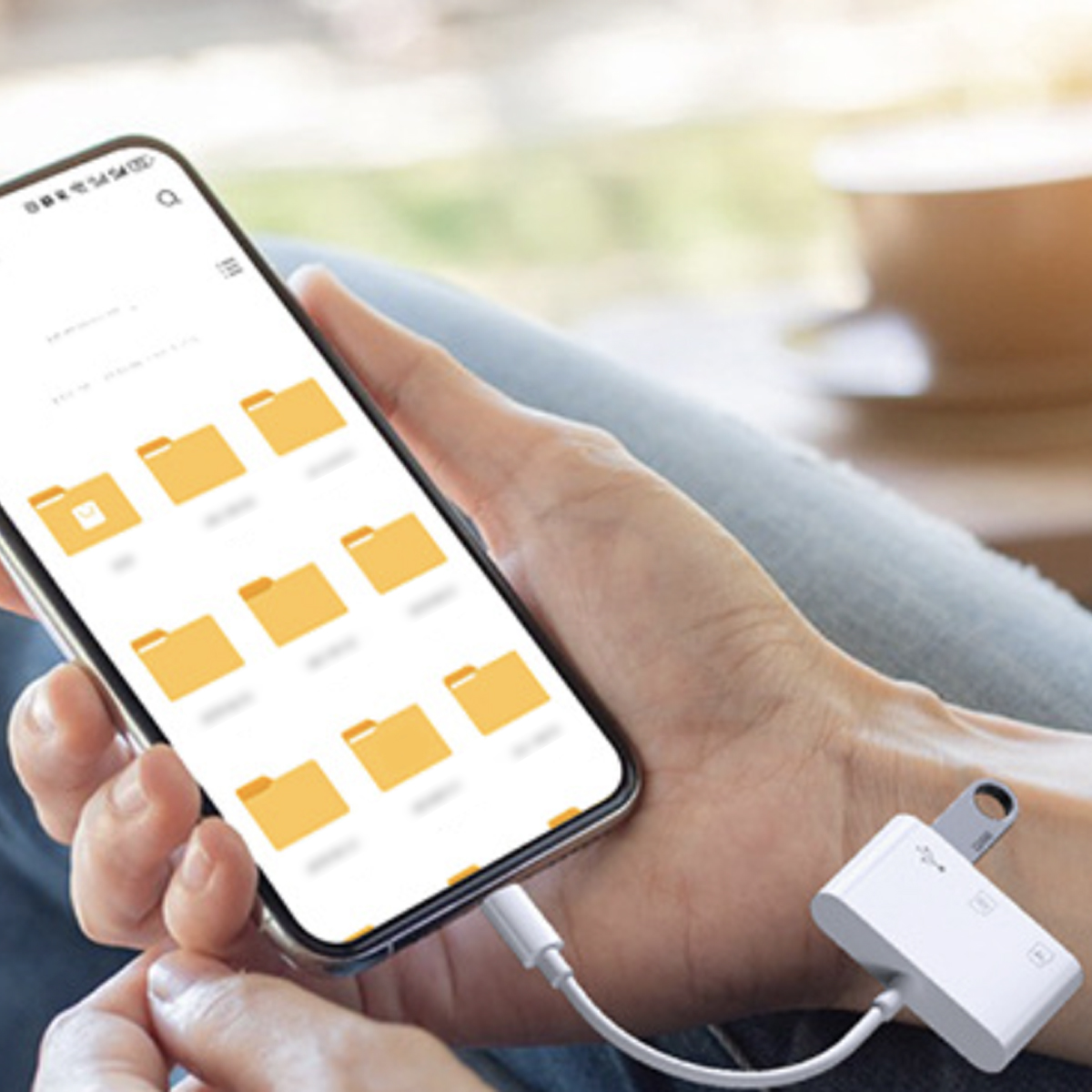 Eine Person hält ein Smartphone, das mit einem weißen Adapter mit USB-Laufwerk und Kabel verbunden ist.
