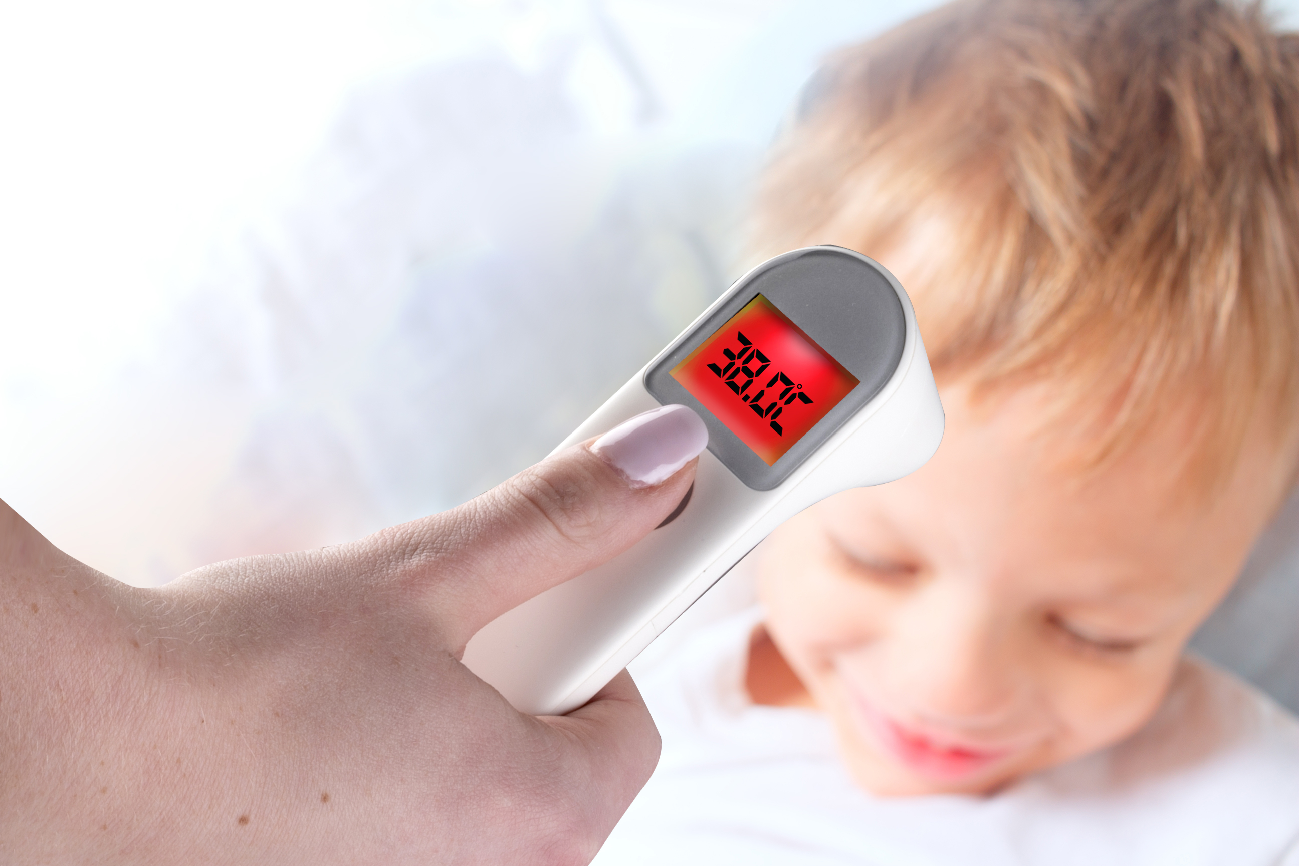 A hand holding a thermometer near a child's face. Thermometer reads 38.0°C.