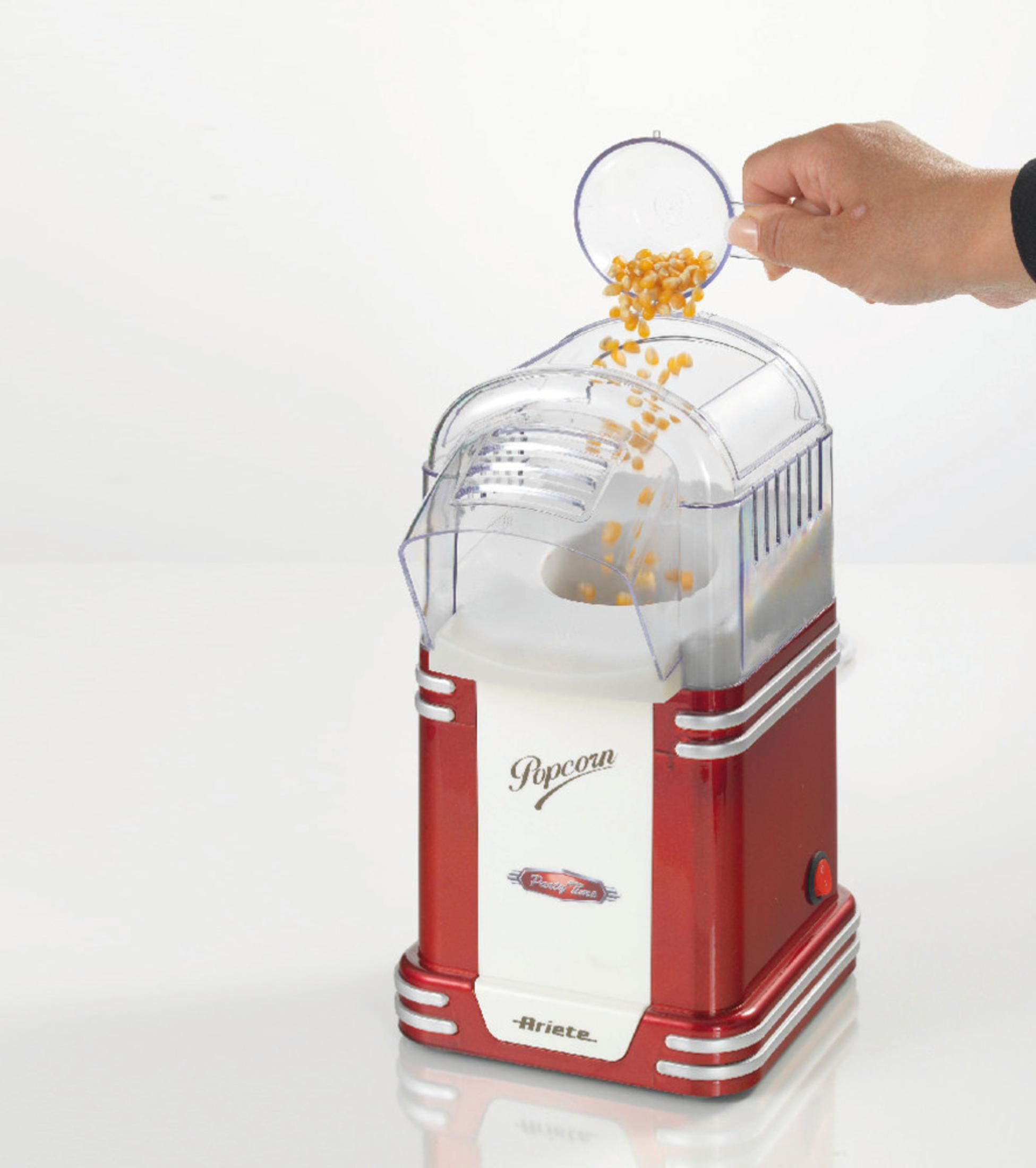 Macchina per popcorn rossa e bianca con chicchi di mais versati da un misurino trasparente.