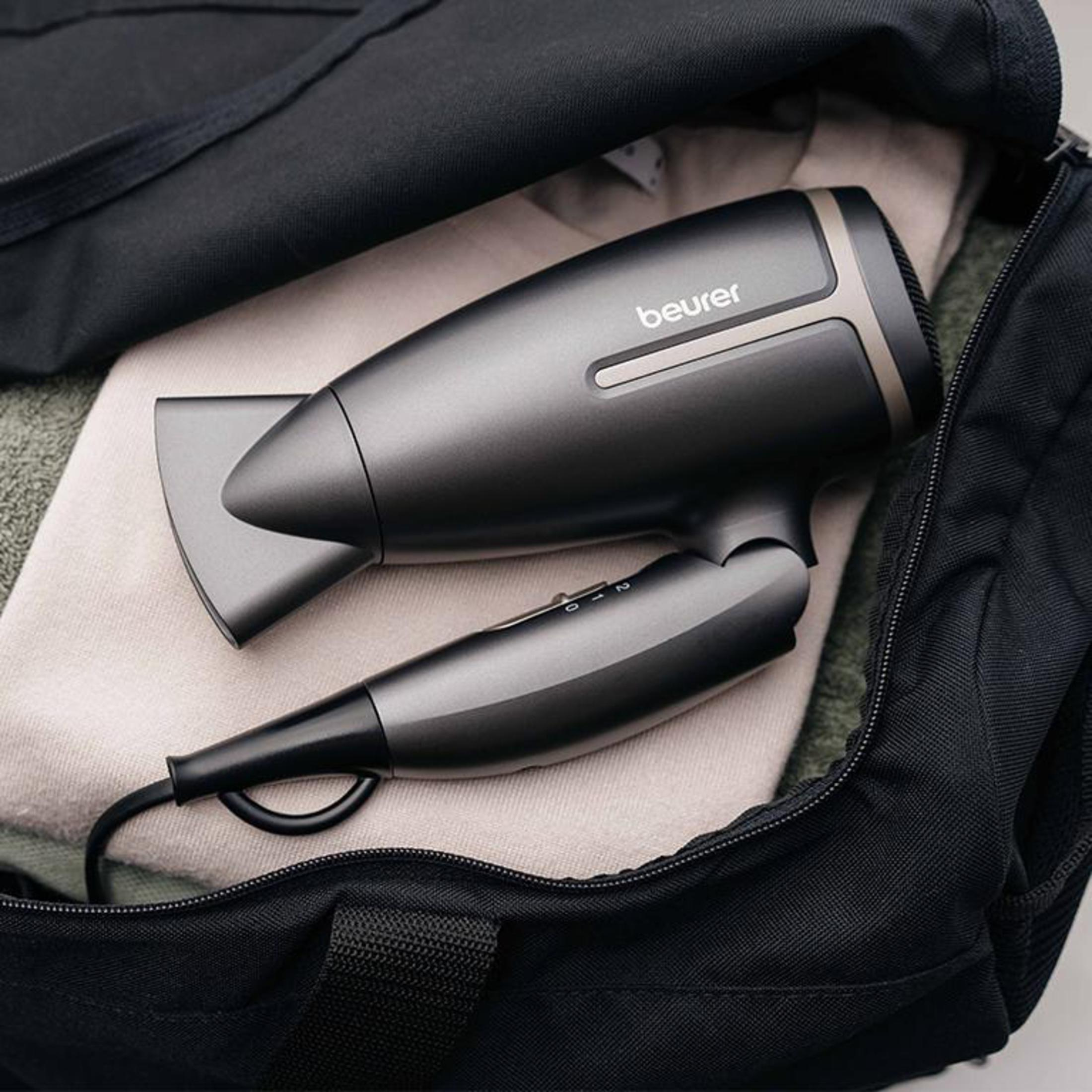 Un asciugacapelli nero all'interno di una borsa nera, accanto a un maglione beige e un asciugamano verde.