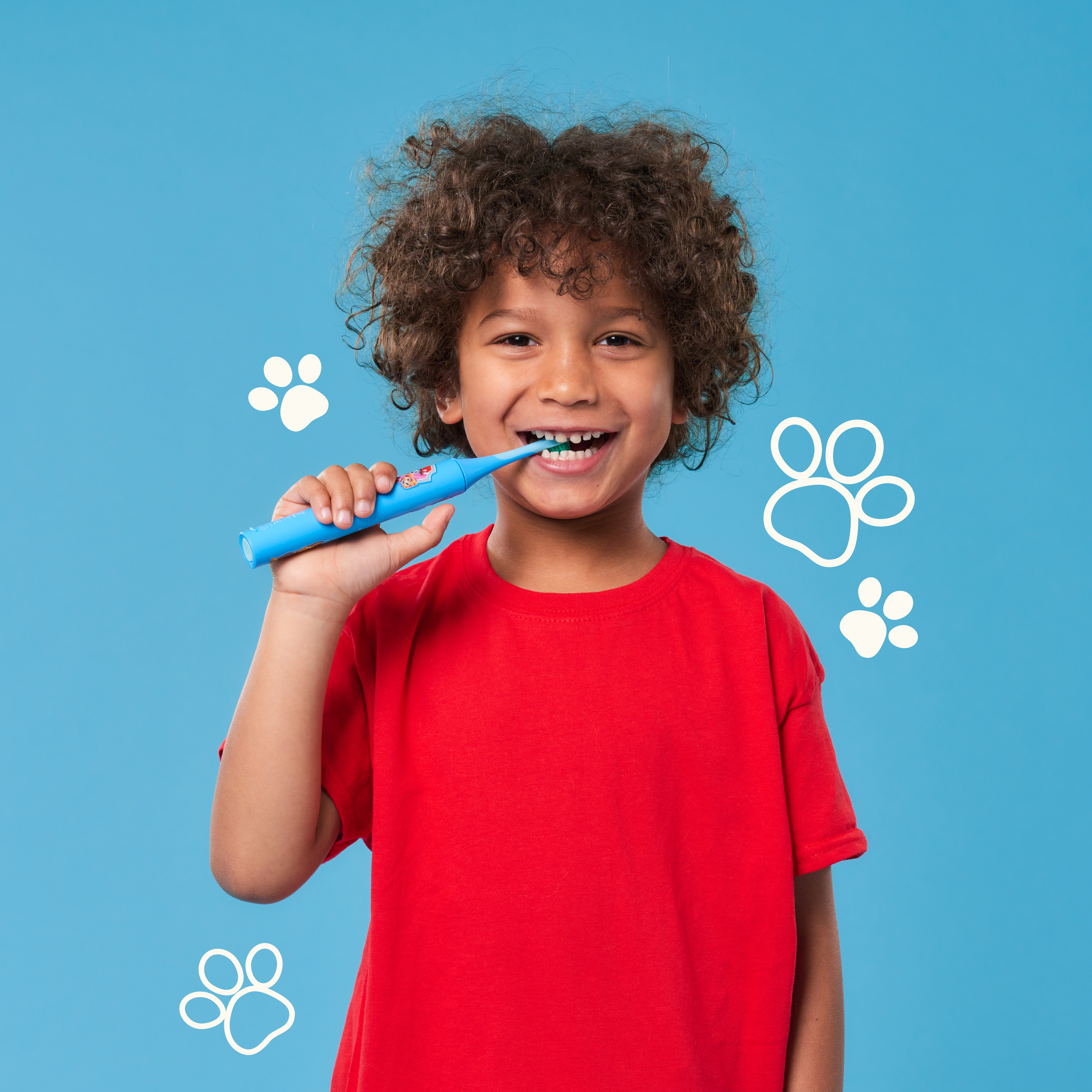 Niño con cabello rizado cepillándose los dientes con un cepillo azul. Fondo azul con huellas blancas.