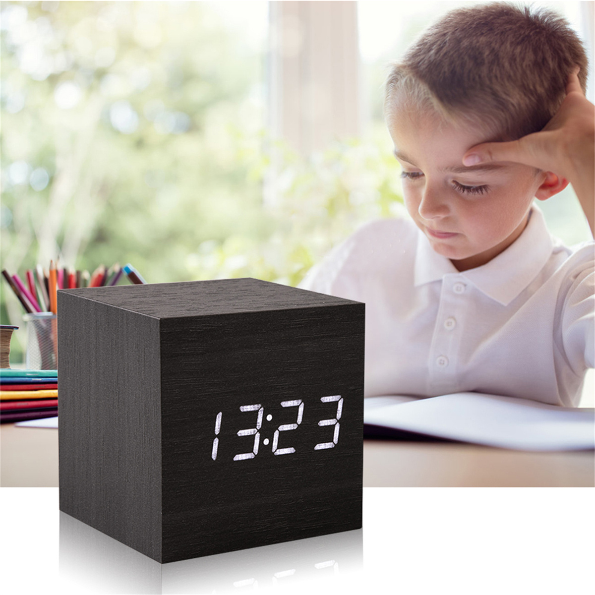 Ein Junge betrachtet eine schwarze Holzquaderuhr, die '13:23' auf einem Tisch anzeigt.
