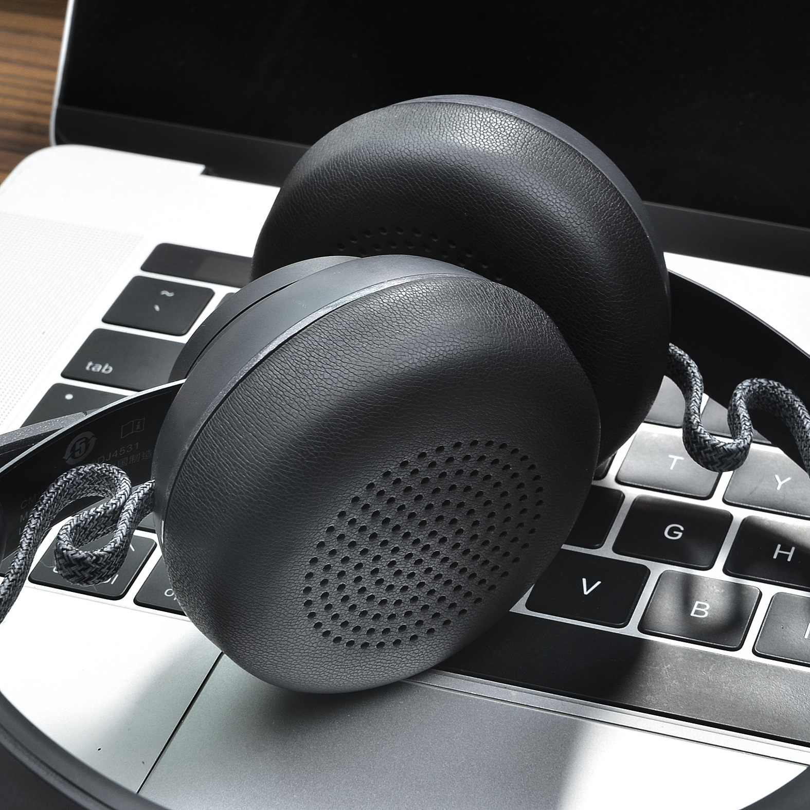 Ciemnoszare słuchawki na klawiaturze laptopa. Widoczny przewód. Słuchawki są na klawiszach.