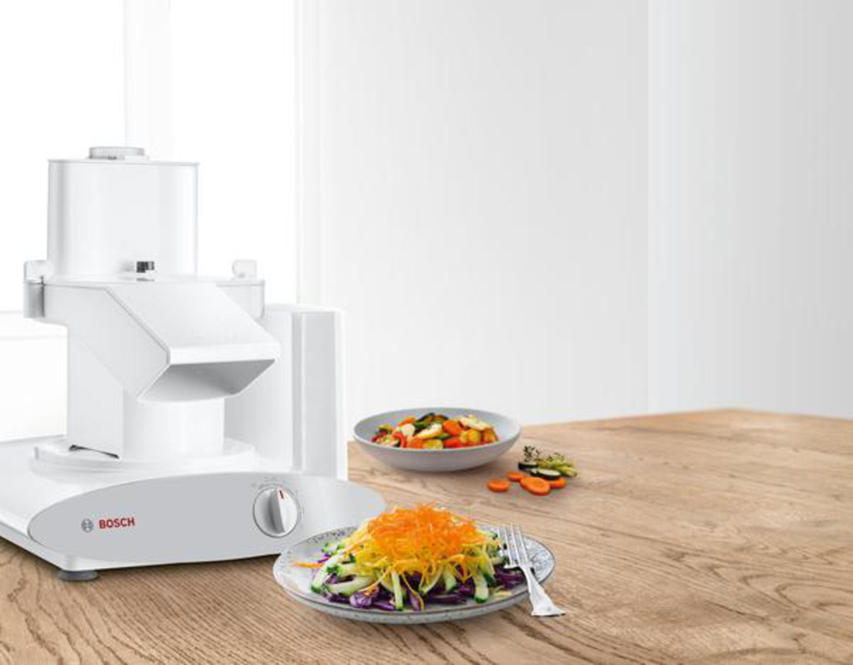 Ein weißer Foodprozessor mit Essen auf einem Teller und einem Holztisch.