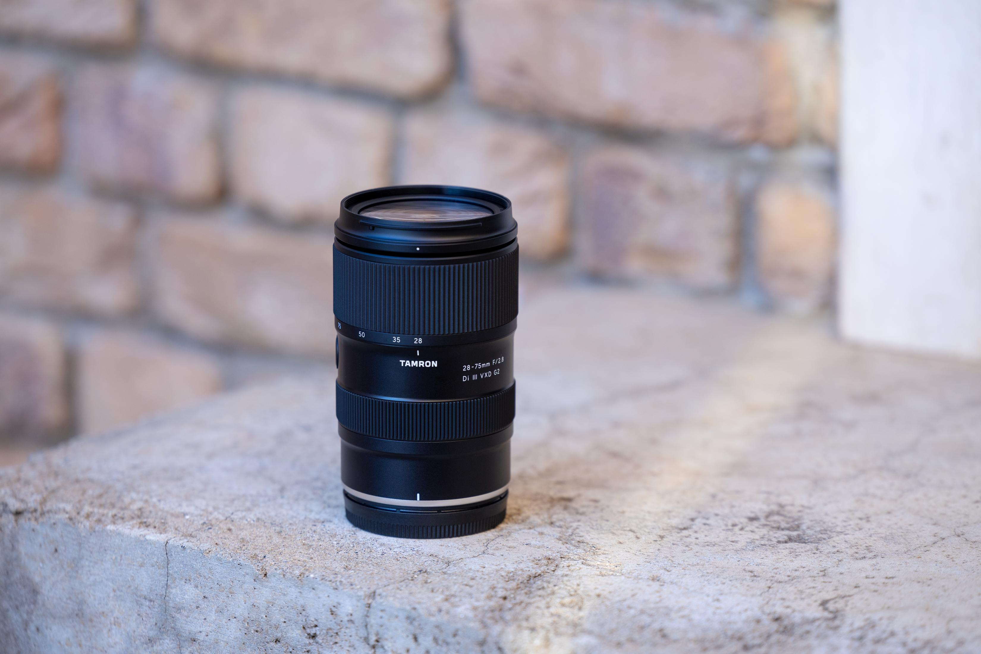 Ein schwarzes Kameraobjektiv auf einer Steinoberfläche. Das Objektiv ist ein Tamron 24-75mm f/2.8 Di III VXD G2.