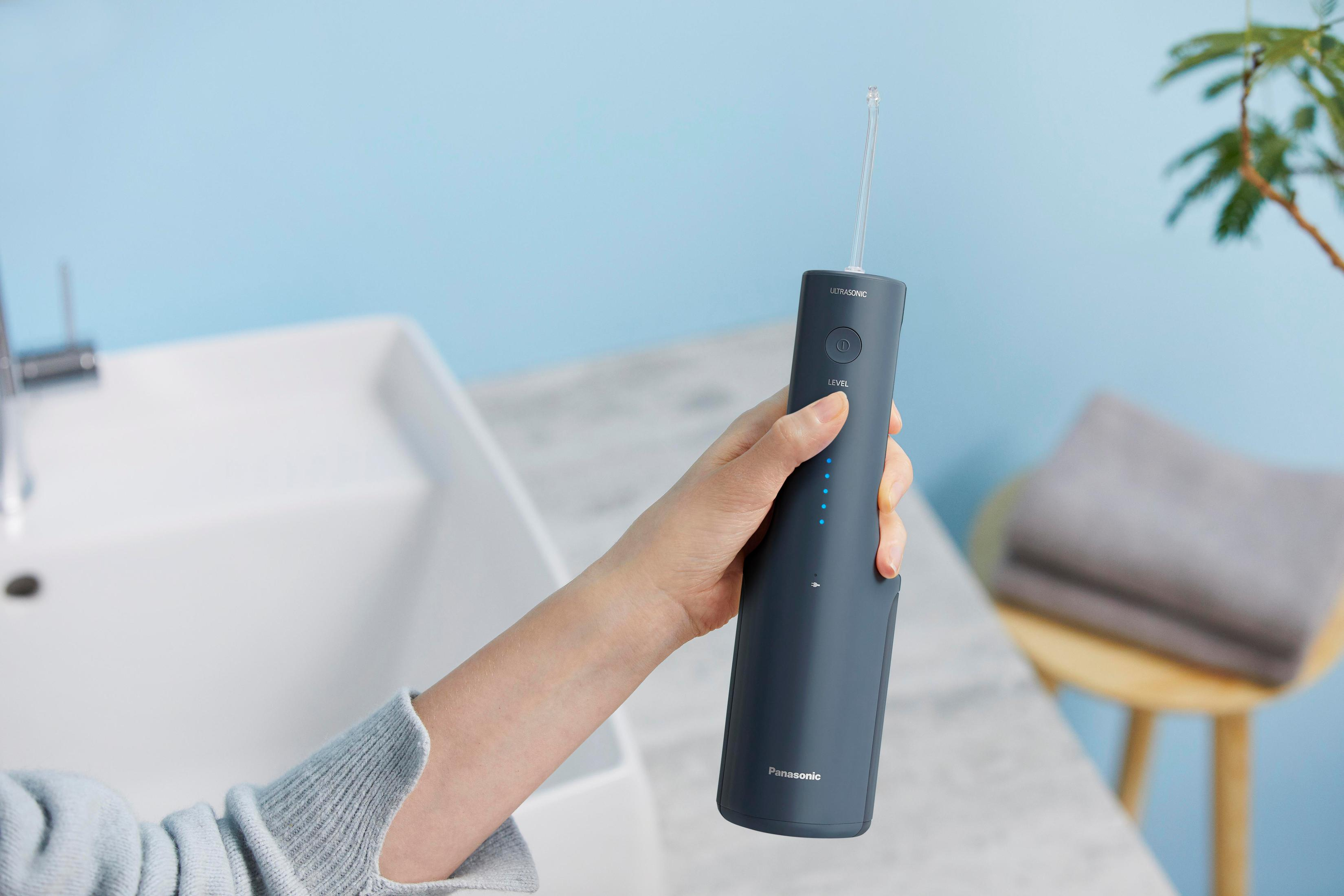 Osoba trzymająca ciemnoszary irygator w łazience.