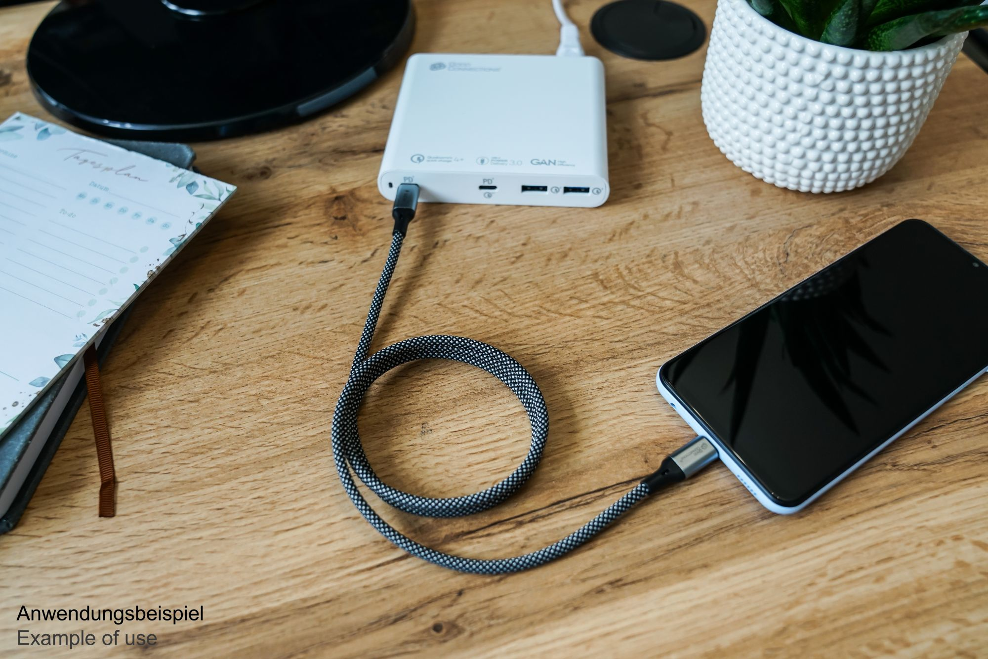 Ein Schreibtisch mit Laptop, Telefon, Powerbank und Notizbuch. Ein Kabel verbindet Telefon und Powerbank.