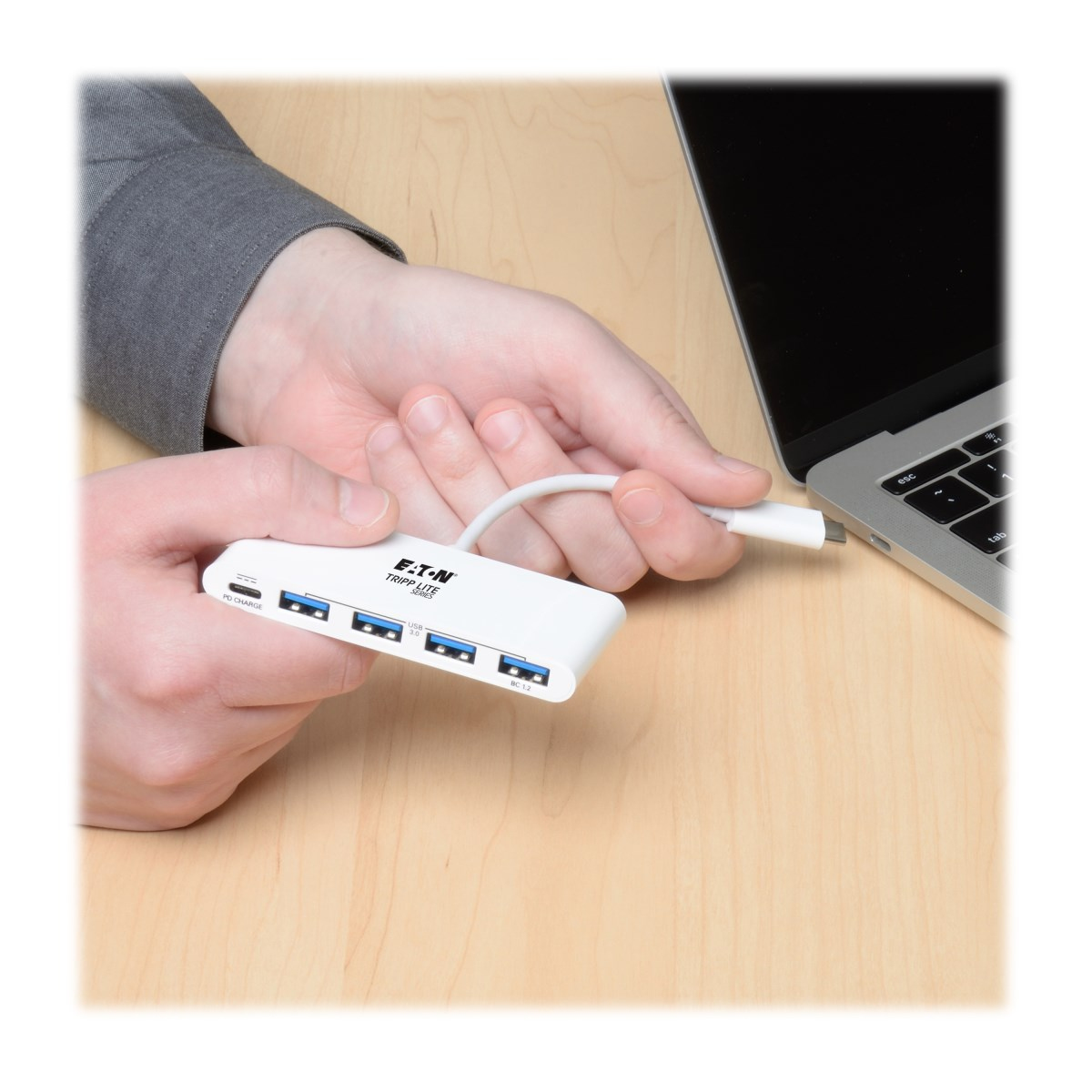 Mano che tiene un hub USB bianco con quattro porte, collegandolo a un laptop.