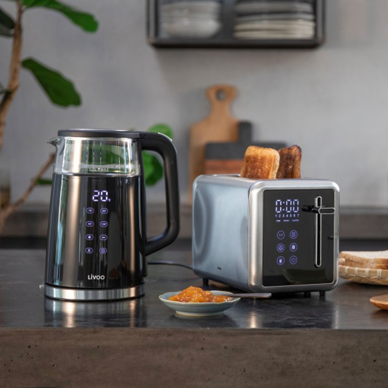 Scena kuchenna: czarny czajnik, toster z tostami i miska dżemu na blacie.