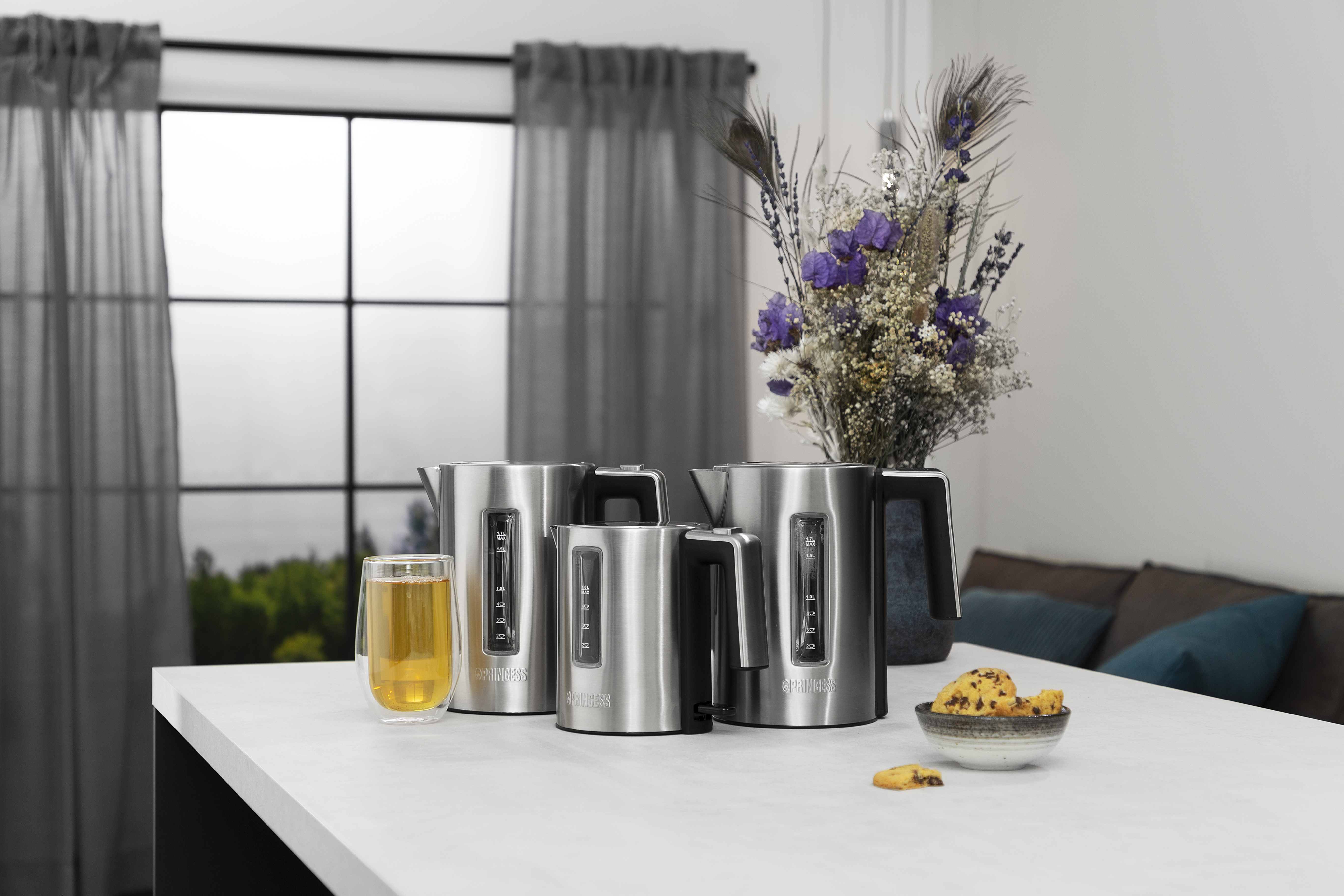 Czajniki ze stali nierdzewnej i szklanka herbaty na białym blacie kuchennym.