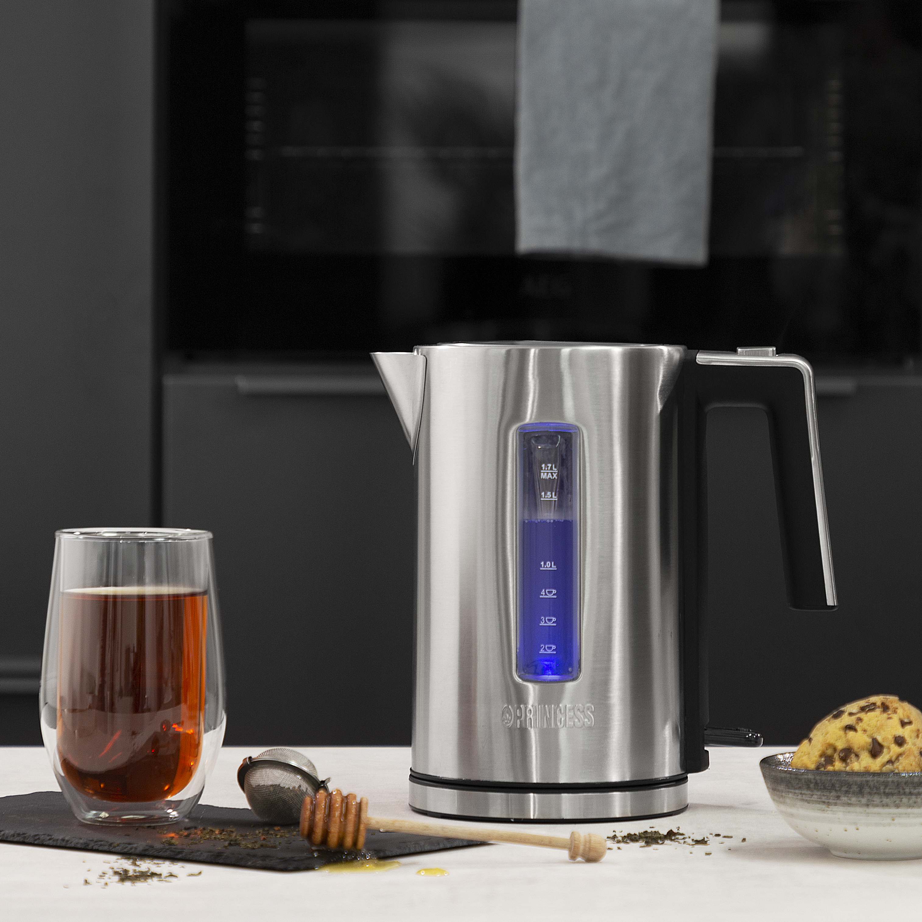Ein elektrischer Wasserkocher aus Edelstahl mit einer Tasse Tee und einem Honiglöffel auf einem Tisch.