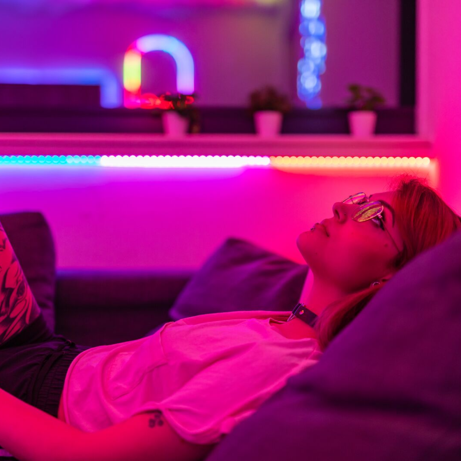 Kobieta leżąca na kanapie, w pokoju oświetlonym neonami.