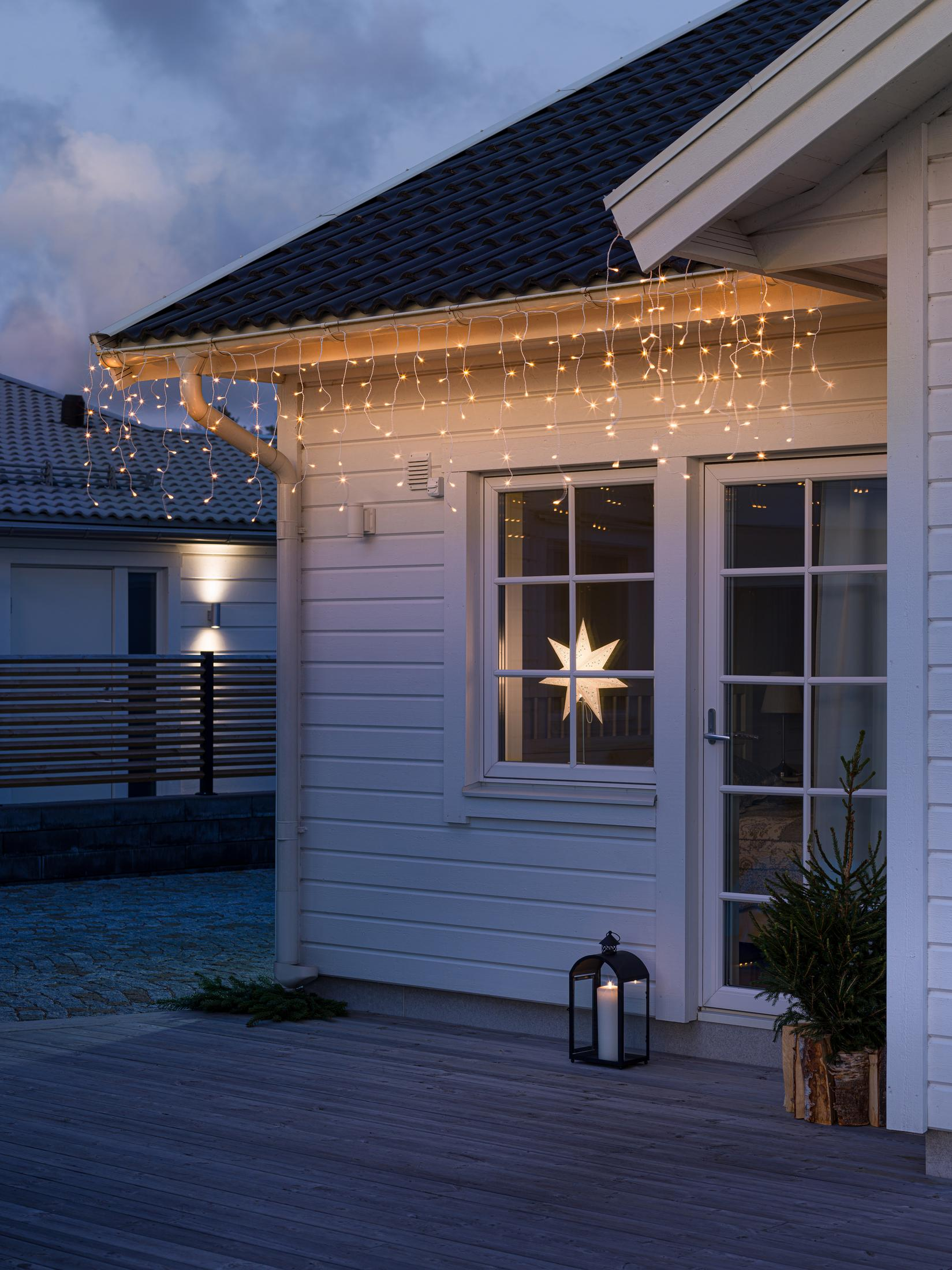 Hausfassade in der Dämmerung mit Lichtern, Weihnachtsbeleuchtung und Stern.