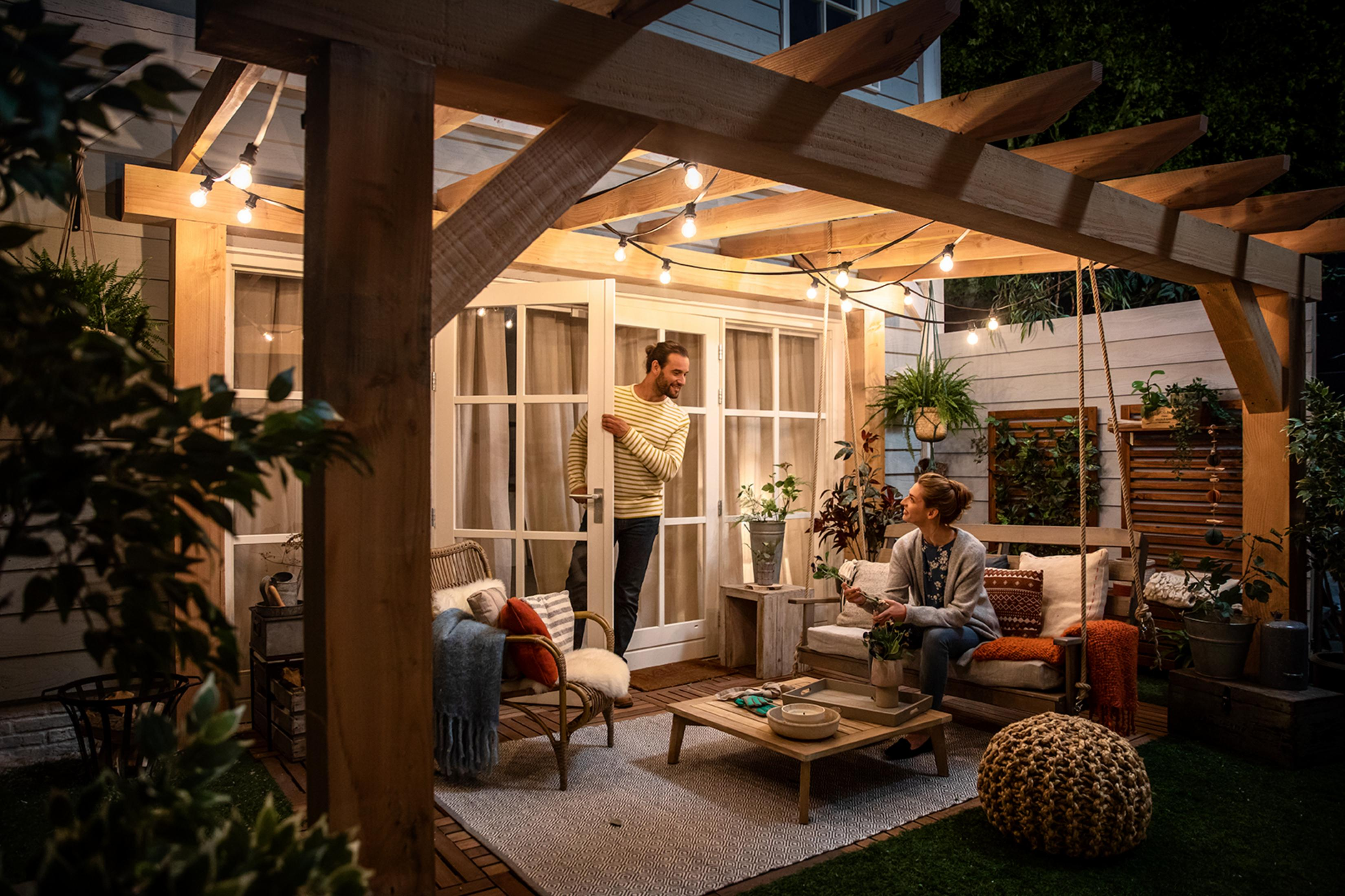 Ein Paar in einem Garten, unter einer Holzpergola mit Lichterketten.
