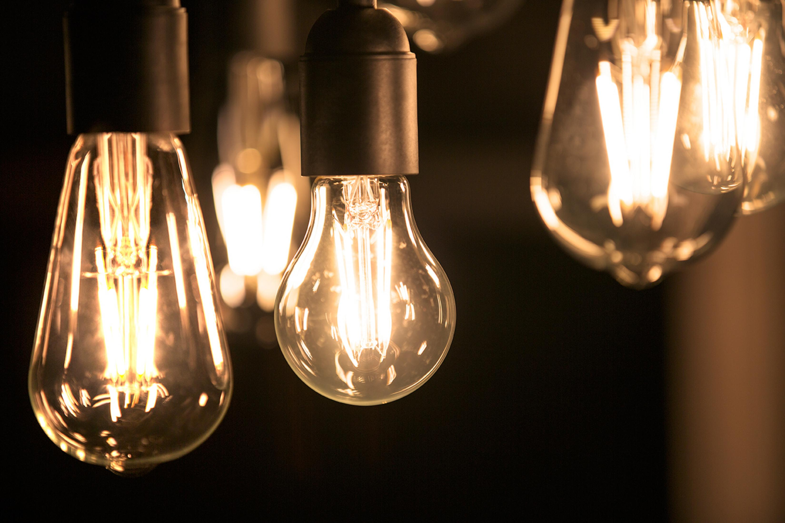 Nahaufnahme von beleuchteten Edison-Glühbirnen, die von der Decke hängen. Dunkler Hintergrund.