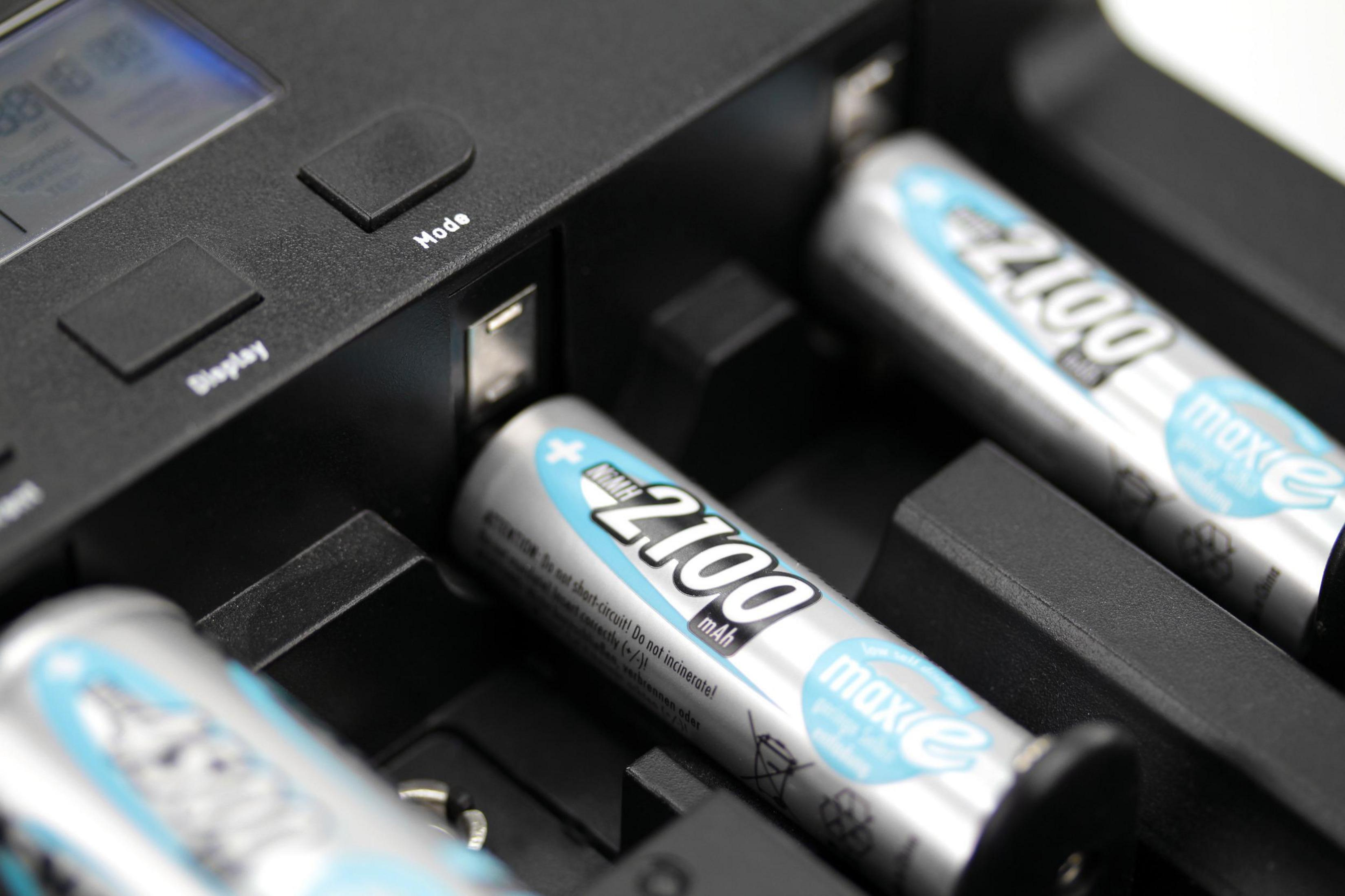 Akkuladegerät mit eingelegten Batterien, schwarz und grau. Weißer Hintergrund.