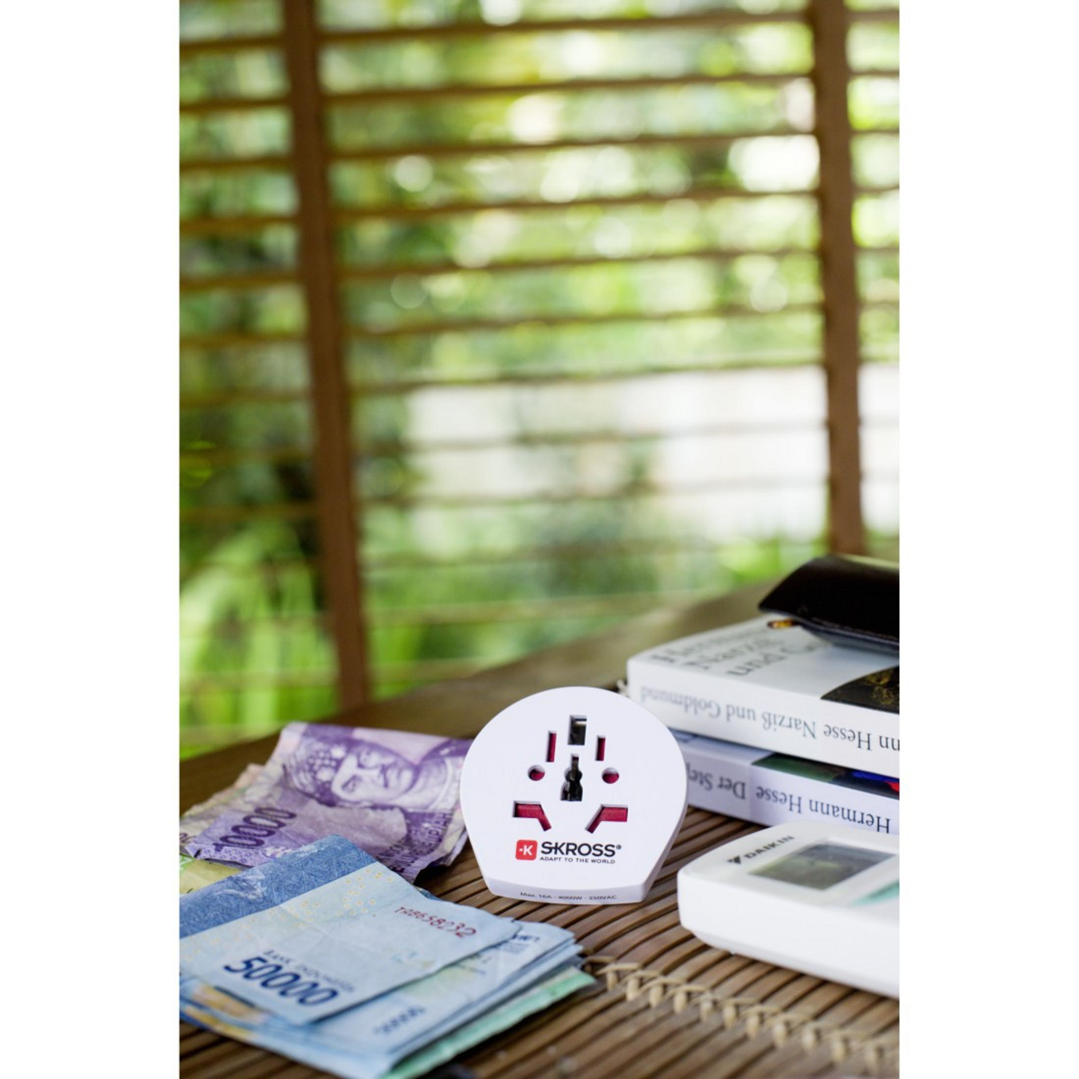 Un adattatore da viaggio bianco con logo rosso e varie porte di ingresso su un tavolo con soldi e libri.