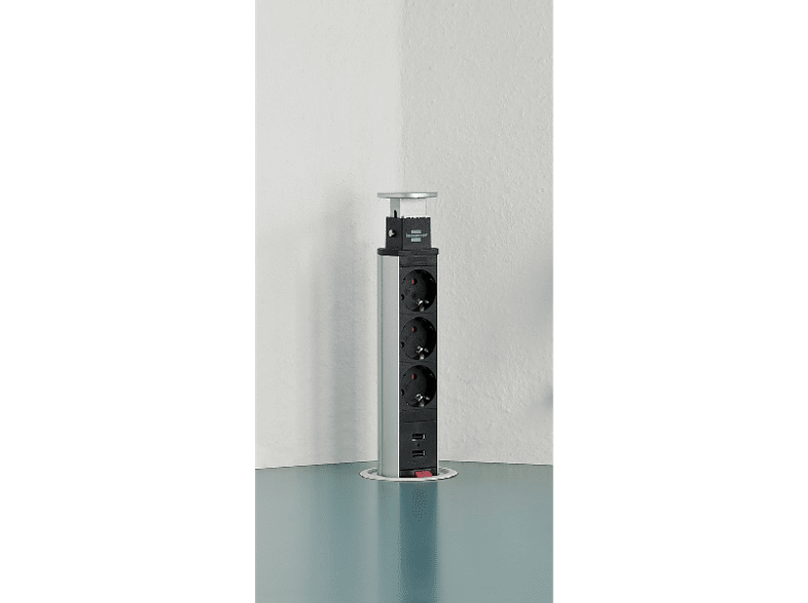 Prolunga di alimentazione argentata con tre prese e due porte USB vicino a un muro.