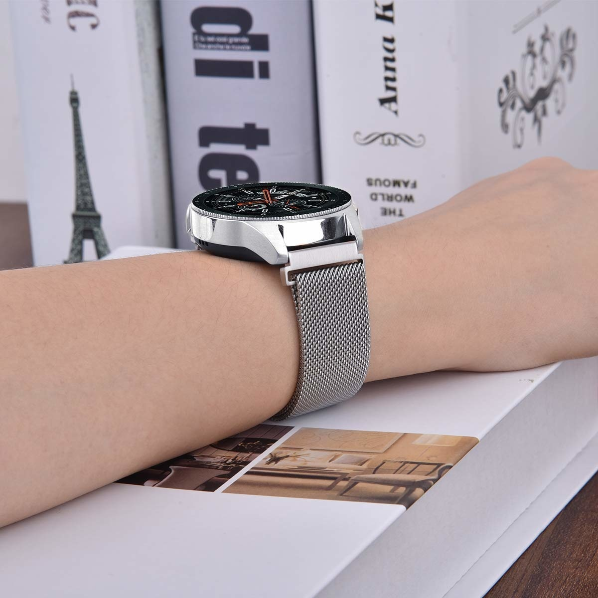 Eine silberne Uhr mit einem Mesh-Armband. Die Uhr liegt auf einem Stapel Bücher.