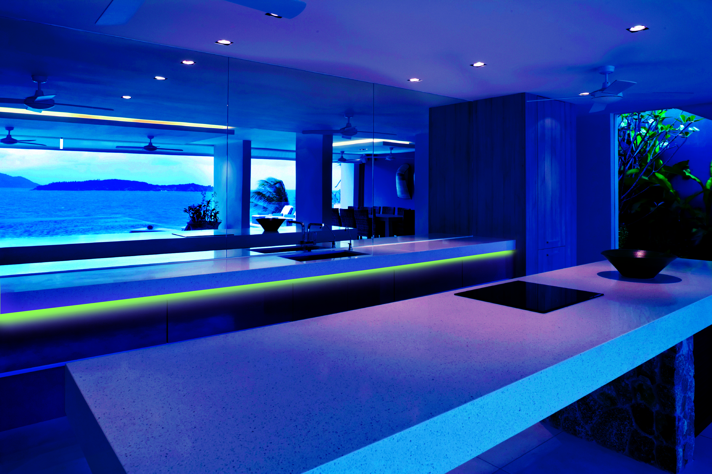 Modern kitchen interior with a blue light design. View from the kitchen to the sea through a window.