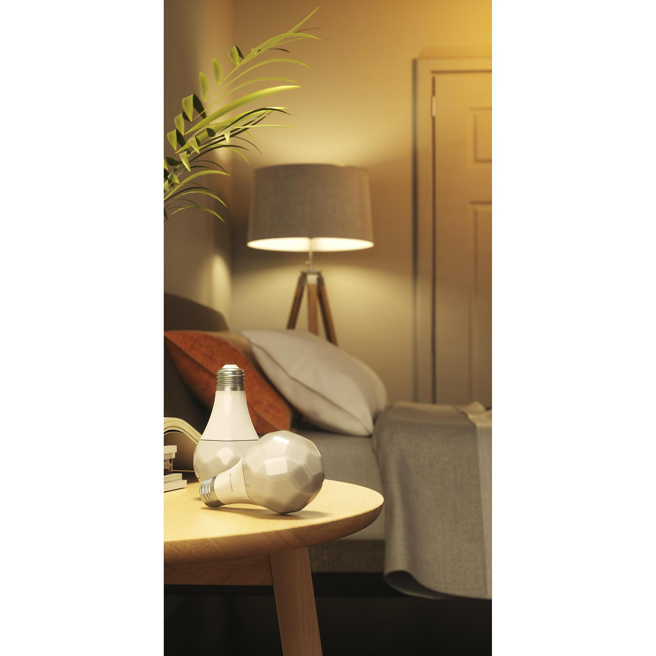 Due lampadine, una accesa su un tavolo, e una lampada sullo sfondo. Illuminazione calda.