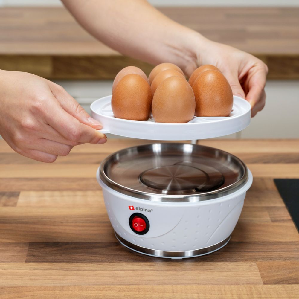 Hands holding a tray with brown eggs over an egg boiler.