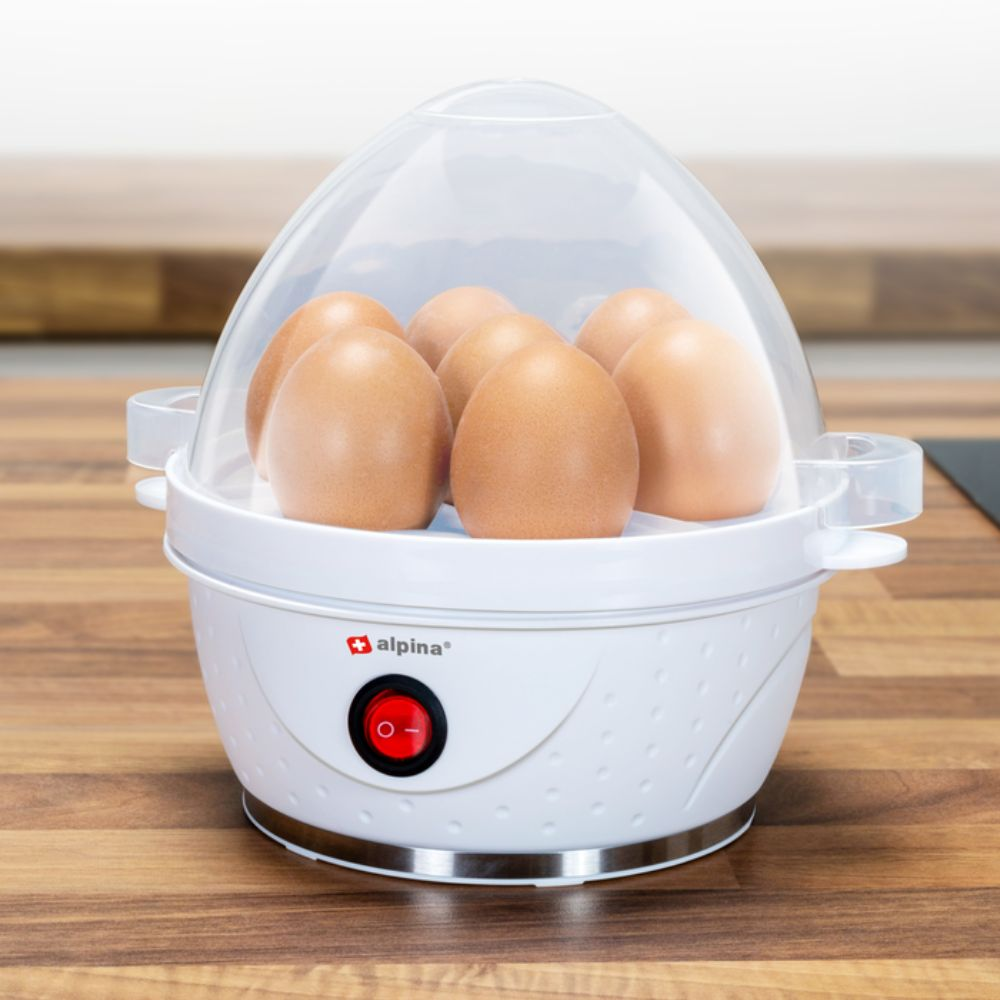 An egg boiler with 6 eggs inside, and a clear lid. The boiler is white with a red power button.