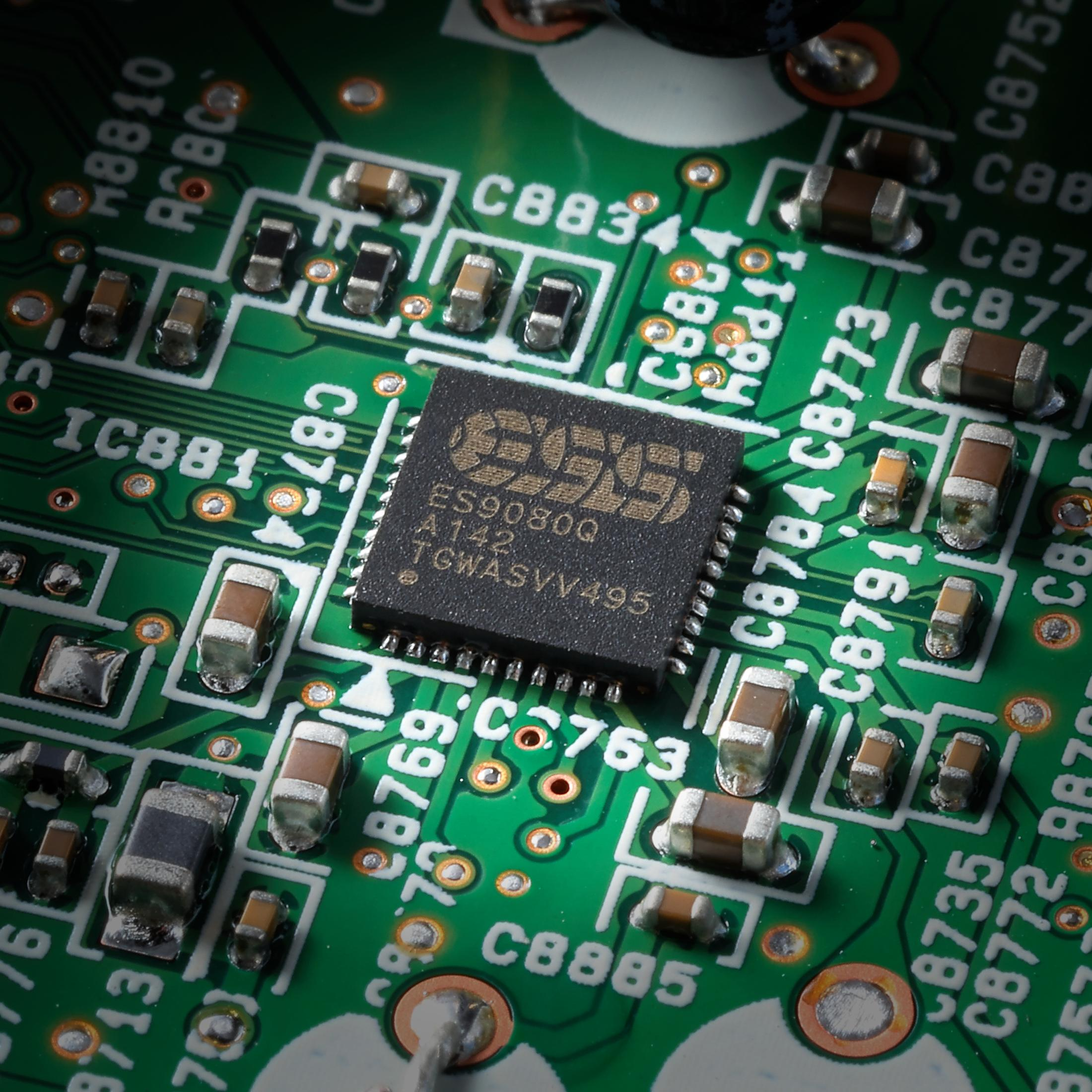 Nahaufnahme einer grünen Platine mit einem schwarzen Chip und Komponenten.