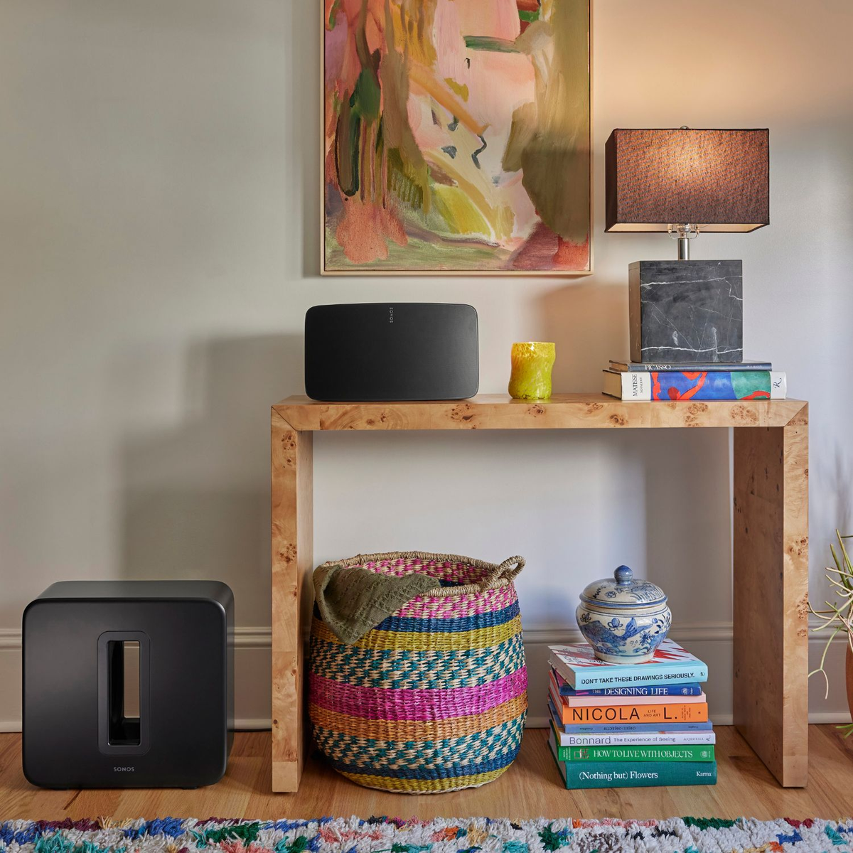 Salon z czarnym głośnikiem, sztuką, lampą, książkami i plecionym koszem.