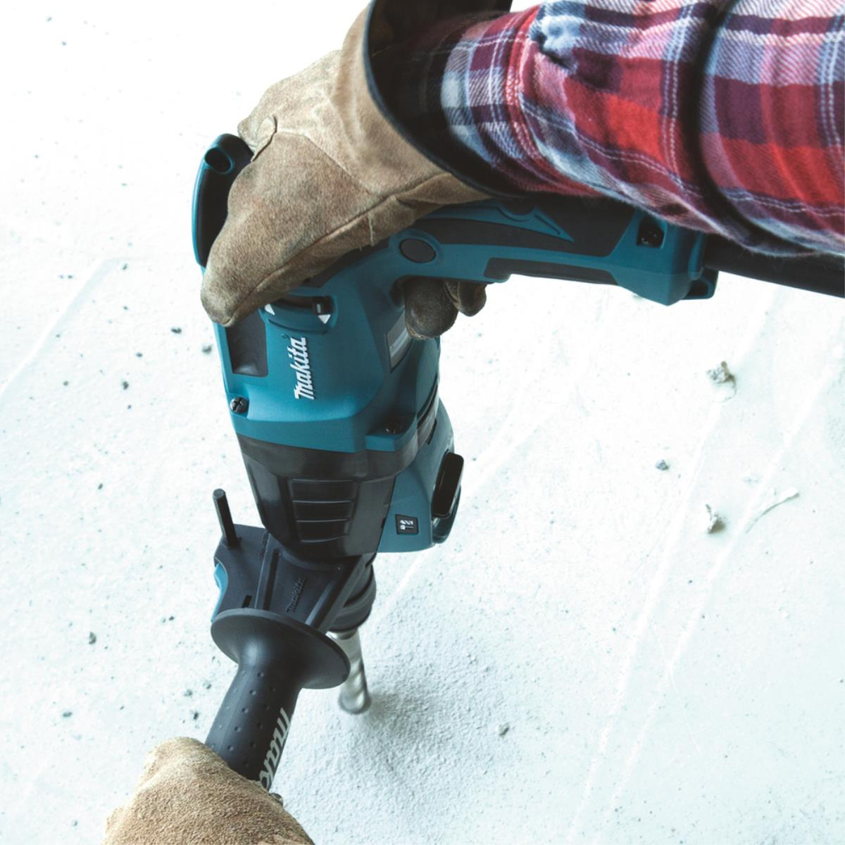Una persona usando un taladro percutor Makita color turquesa sobre una superficie de hormigón.
