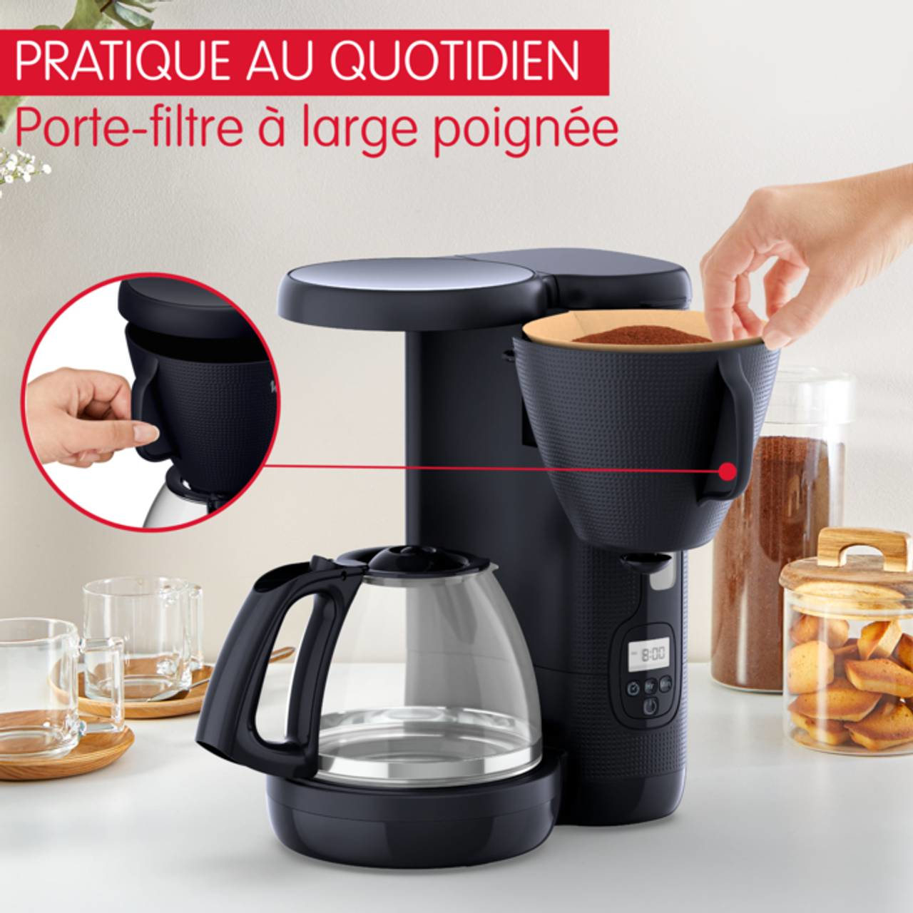 Black coffee maker with a large handle. A hand is placing a filter in the machine.