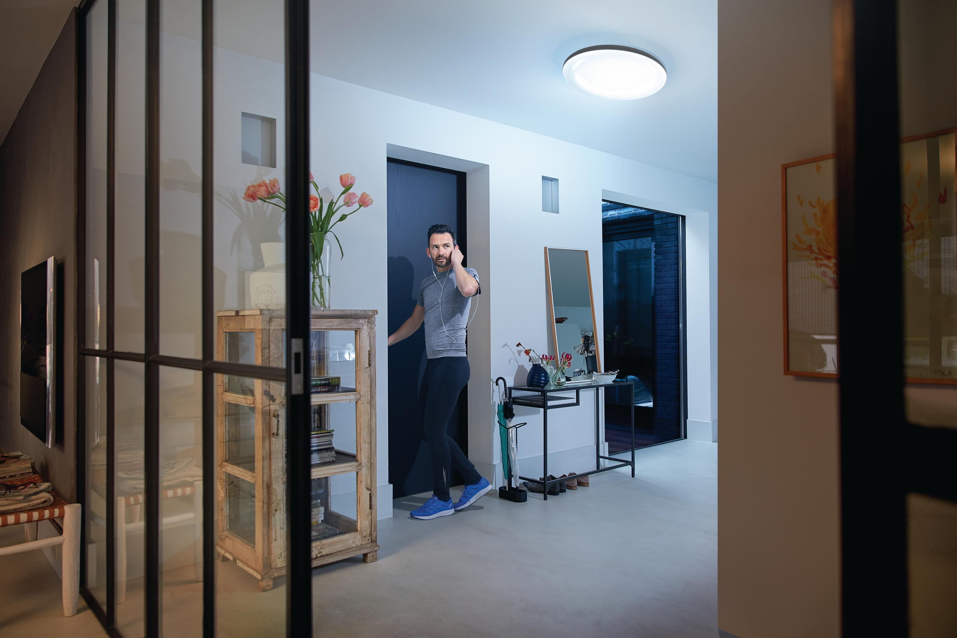 Un uomo con camicia grigia e pantaloni neri attraversa una porta d'ingresso moderna.