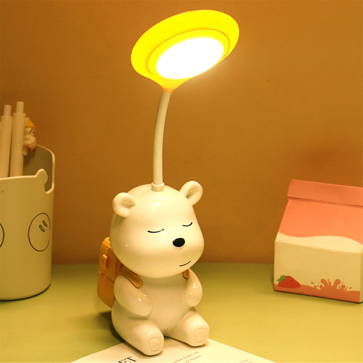 Eine weiße bärenförmige Lampe mit gelbem Licht und Rucksack auf dem Schreibtisch.
