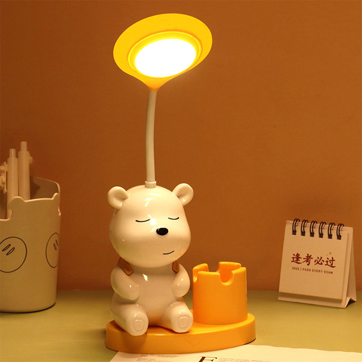 Eine bärenförmige Lampe mit gelbem Schirm und Stifthalter, sowie ein Schreibtischkalender.