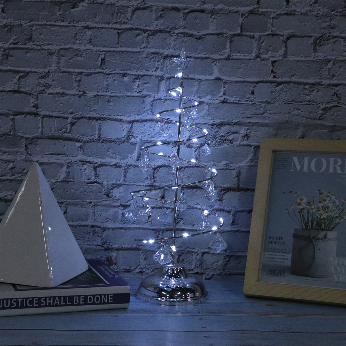 Weihnachtsbaum mit weißen Lichtern und Ornamenten auf einem Tisch. Ziegelwand im Hintergrund.