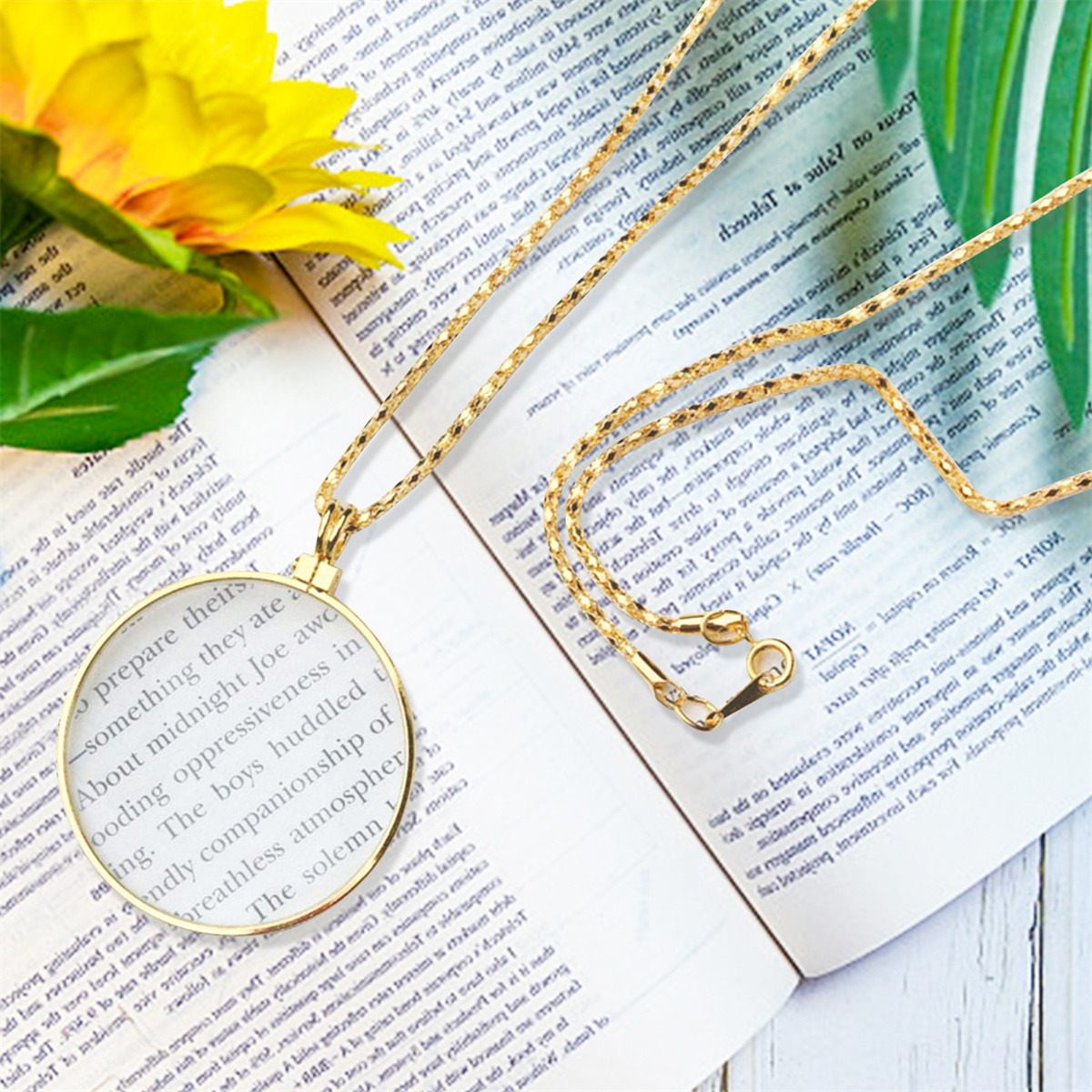 Eine goldene Halskette mit einem Lupenanhänger, die auf einem Buch mit Text liegt, mit einer gelben Blume.