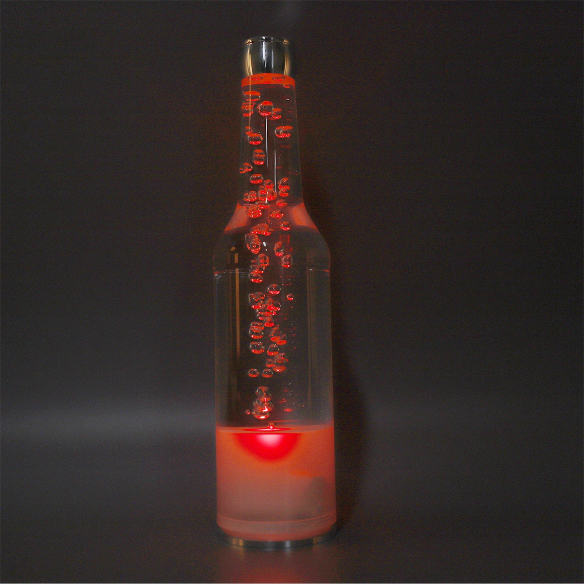 Eine hohe Glasflasche mit roten Blasen im Inneren, auf dunklem Hintergrund. Es gibt einen roten Sockel.