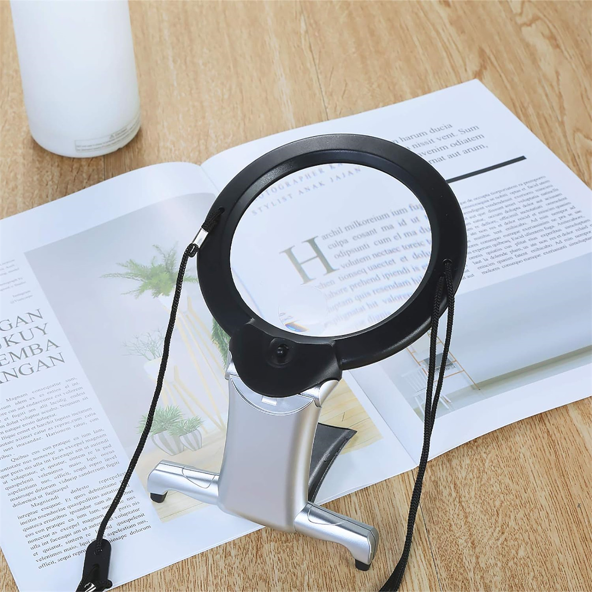 Lupe über einem offenen Buch. Das Glas ist schwarz und silber mit einem Licht. Der Hintergrund ist ein Holztisch.
