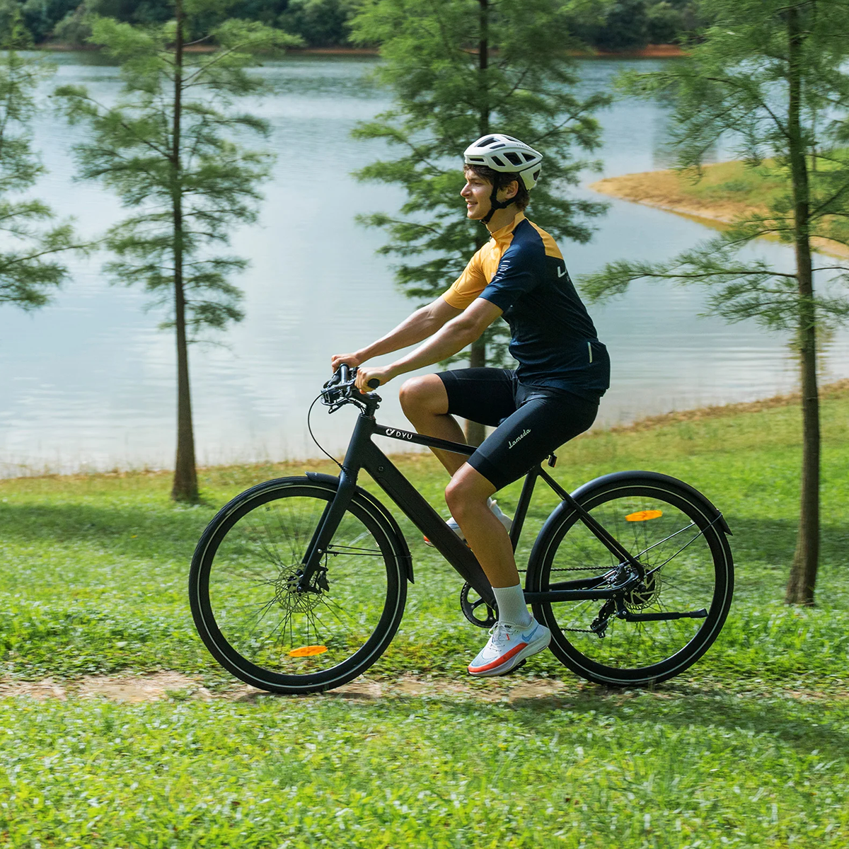 Mężczyzna jedzie czarnym rowerem ścieżką w pobliżu jeziora. Ma na sobie kask i odzież sportową.