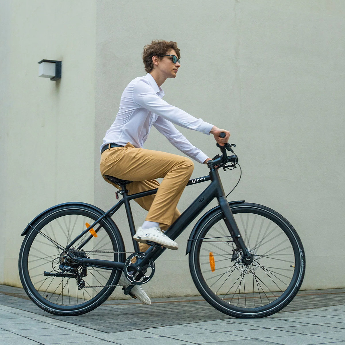 Mężczyzna jadący czarnym rowerem elektrycznym na ulicy. Rower ma pomarańczowe odblaski.
