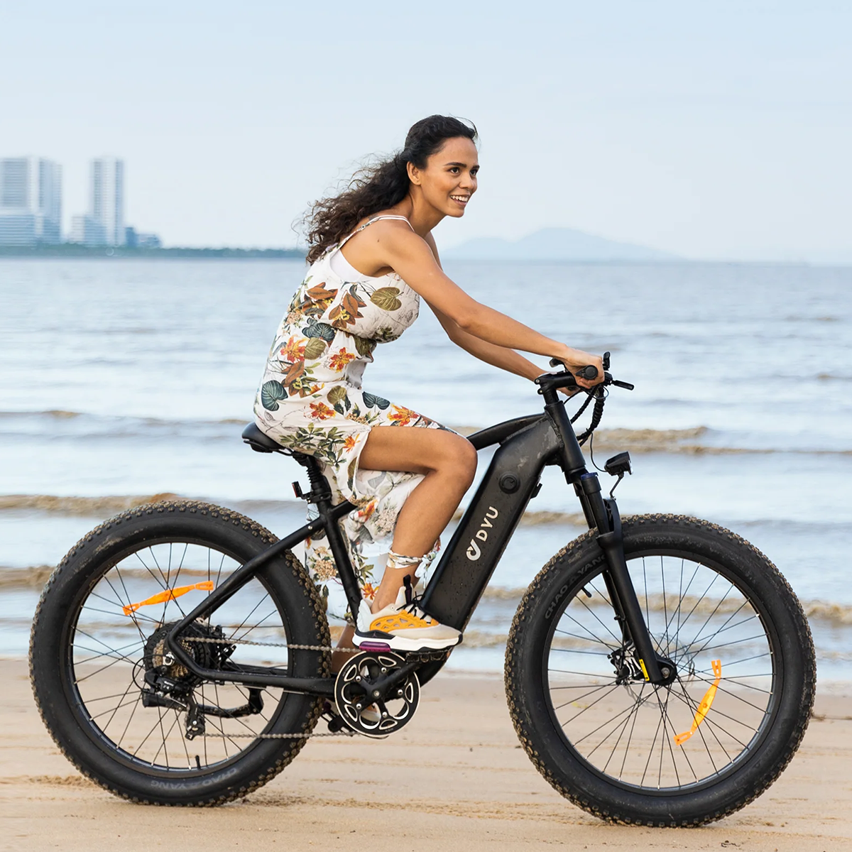 Kobieta na czarnym rowerze elektrycznym DVU, jadąca po plaży.