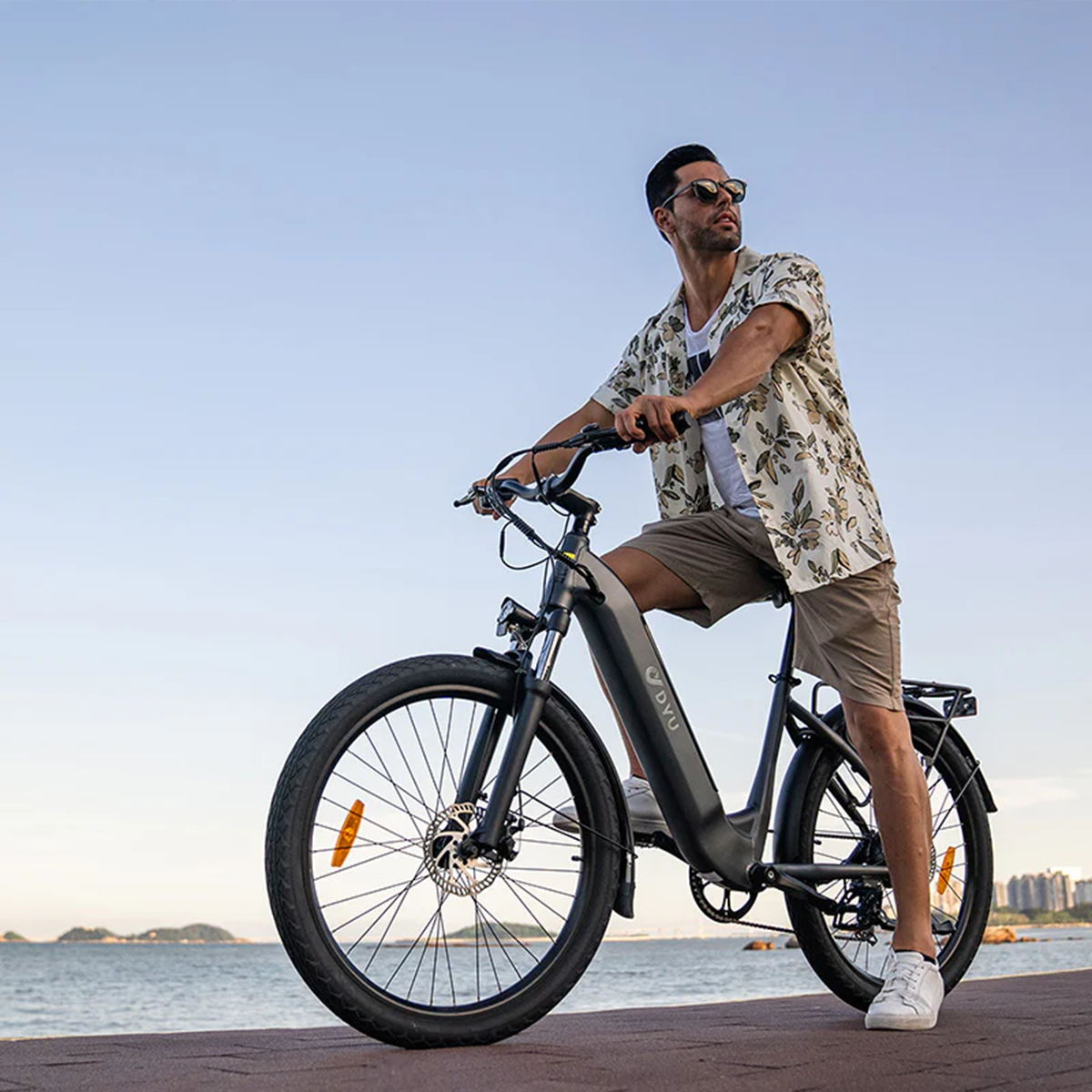 Mężczyzna jadący czarnym rowerem elektrycznym po utwardzonej ścieżce nad oceanem.