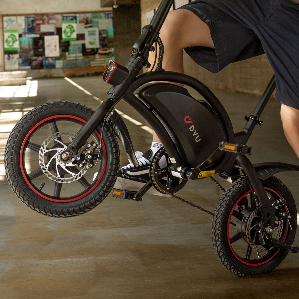 Osoba jedzie czarnym rowerem elektrycznym z czerwonymi akcentami. Rower ma logo Dvu.