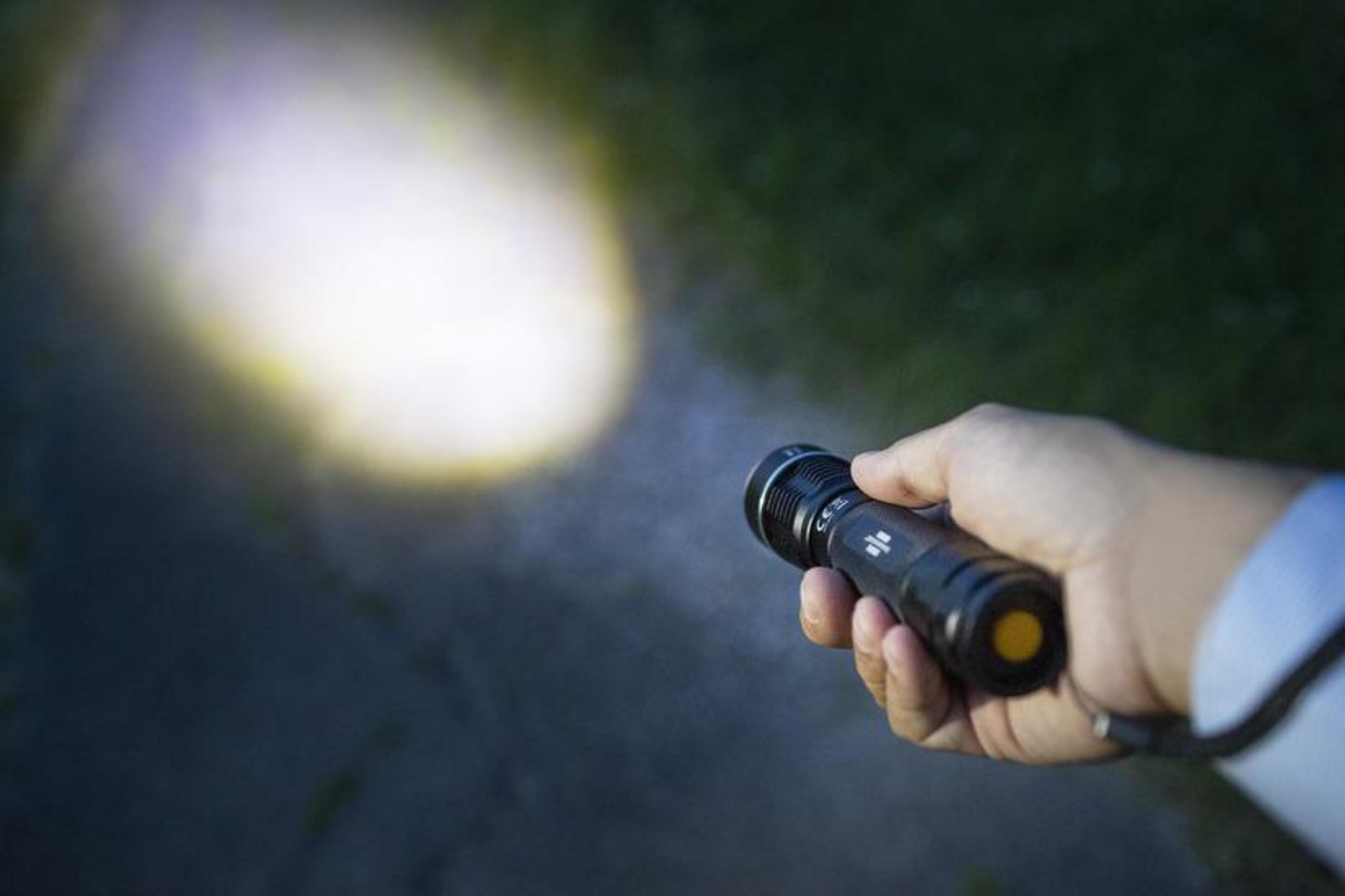 Eine Hand hält eine schwarze Taschenlampe mit hellem Lichtstrahl.